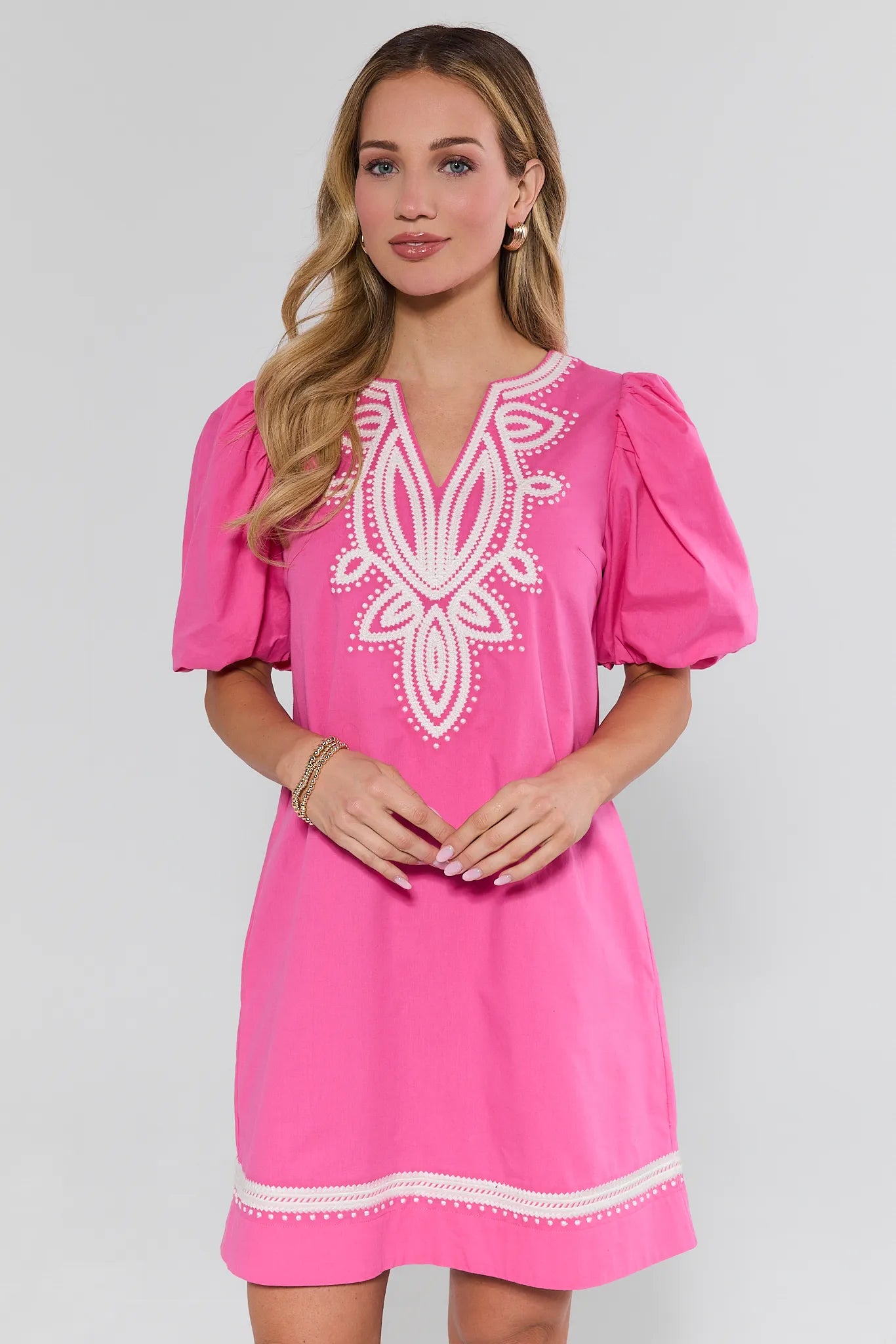 Woman wearing a pink dress with white embroidery on a light gray background