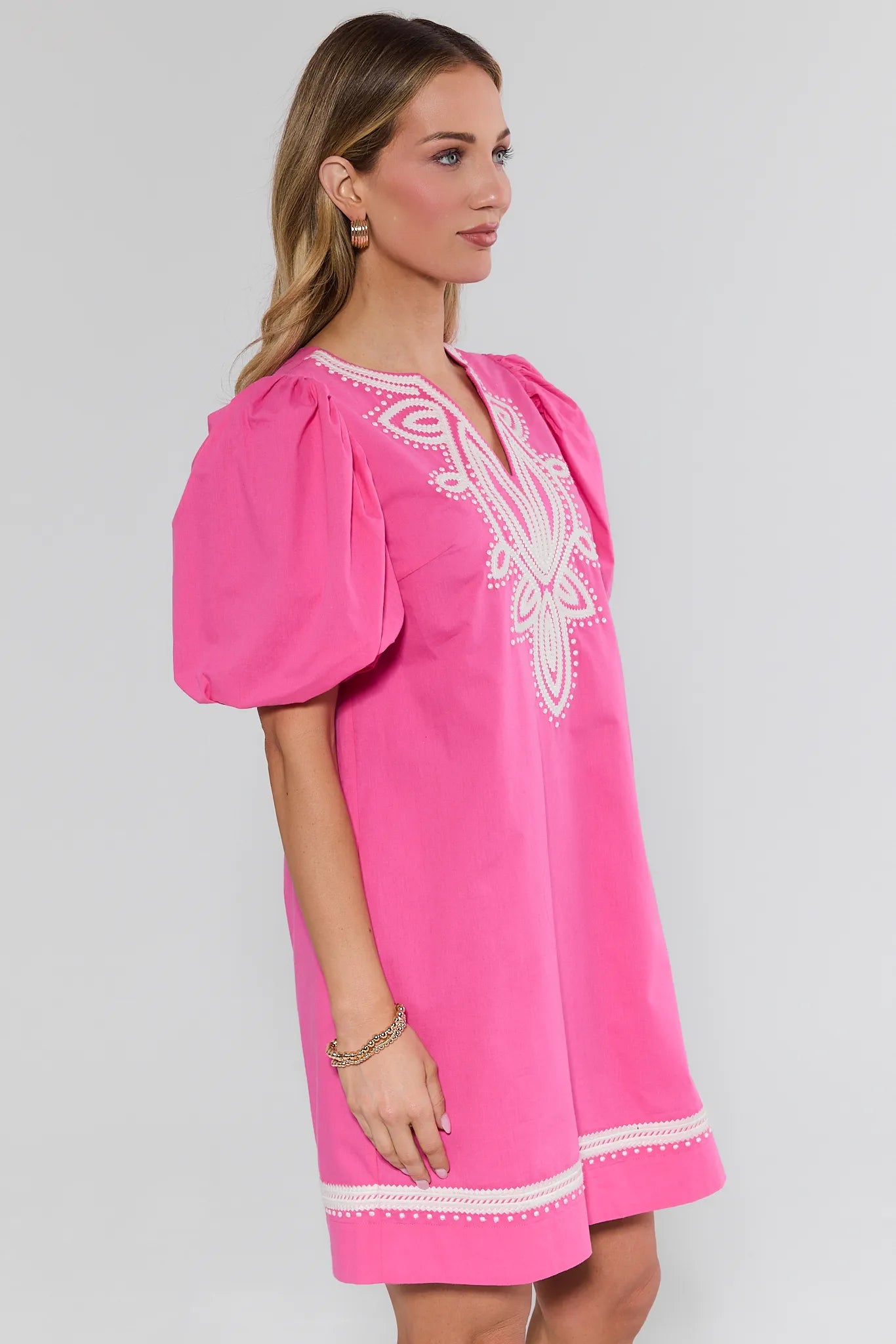 Woman wearing a pink dress with white embroidery on a gray background