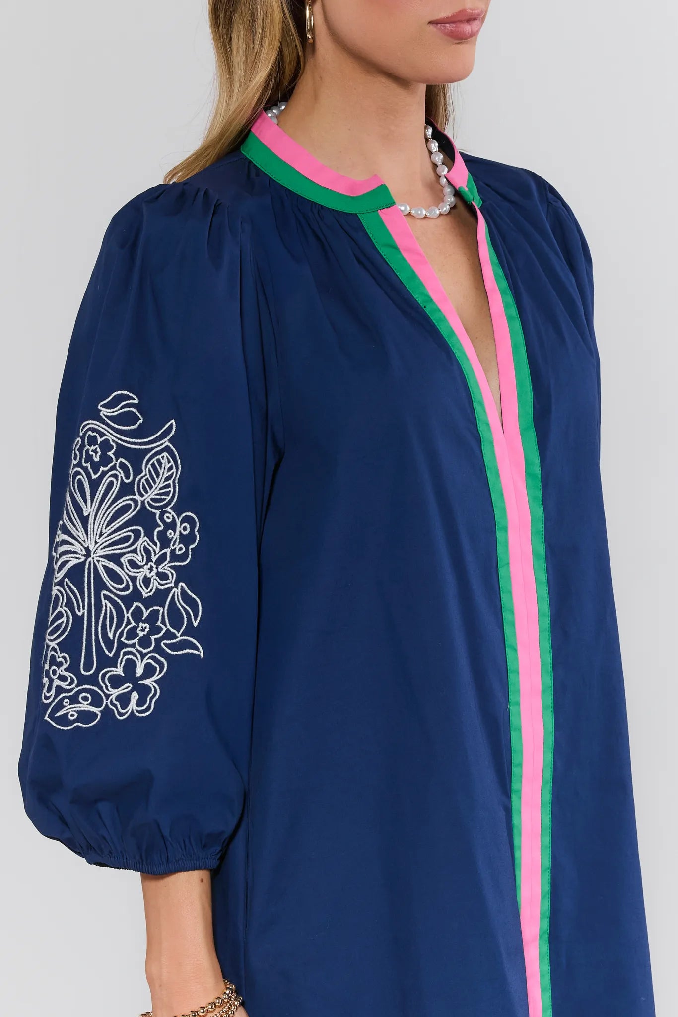 Navy blue dress with floral embroidery and pink trim on a white background