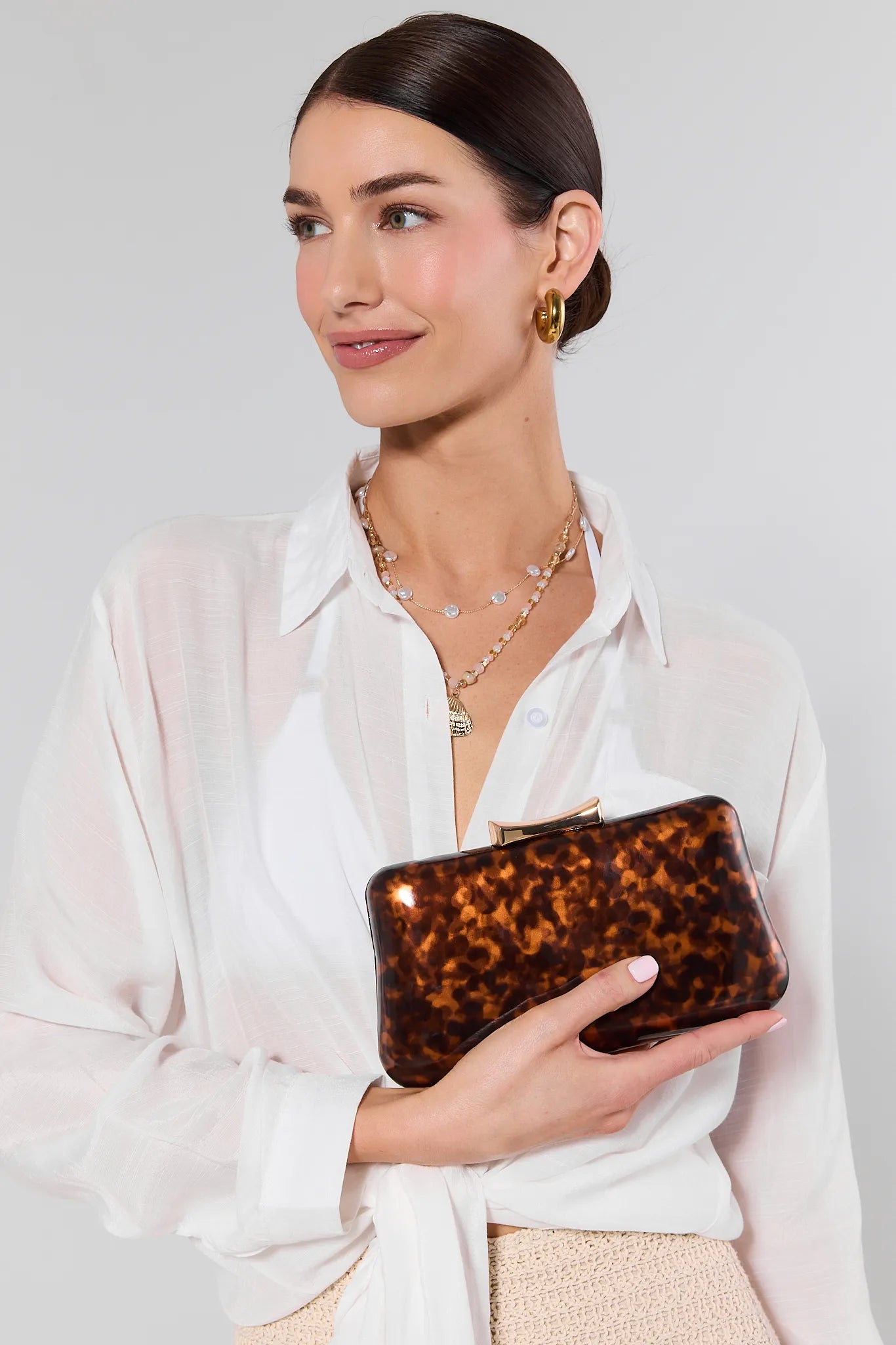 Woman holding a tortoiseshell clutch against a plain background