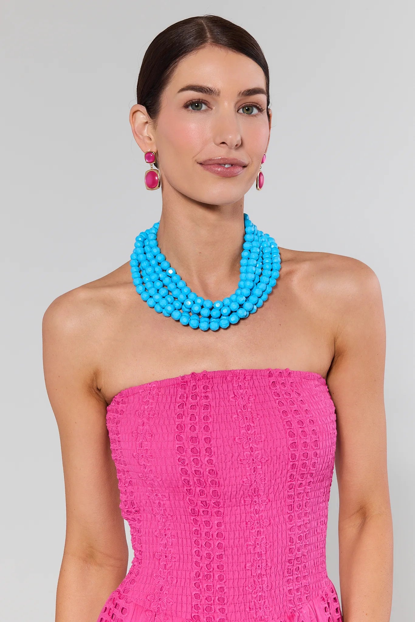 Woman wearing a bright pink strapless dress with a blue necklace against a gray background