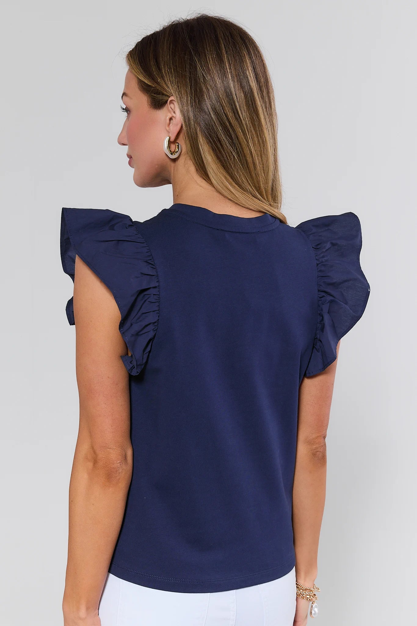 Woman wearing a navy blue top with ruffled sleeves on a plain background
