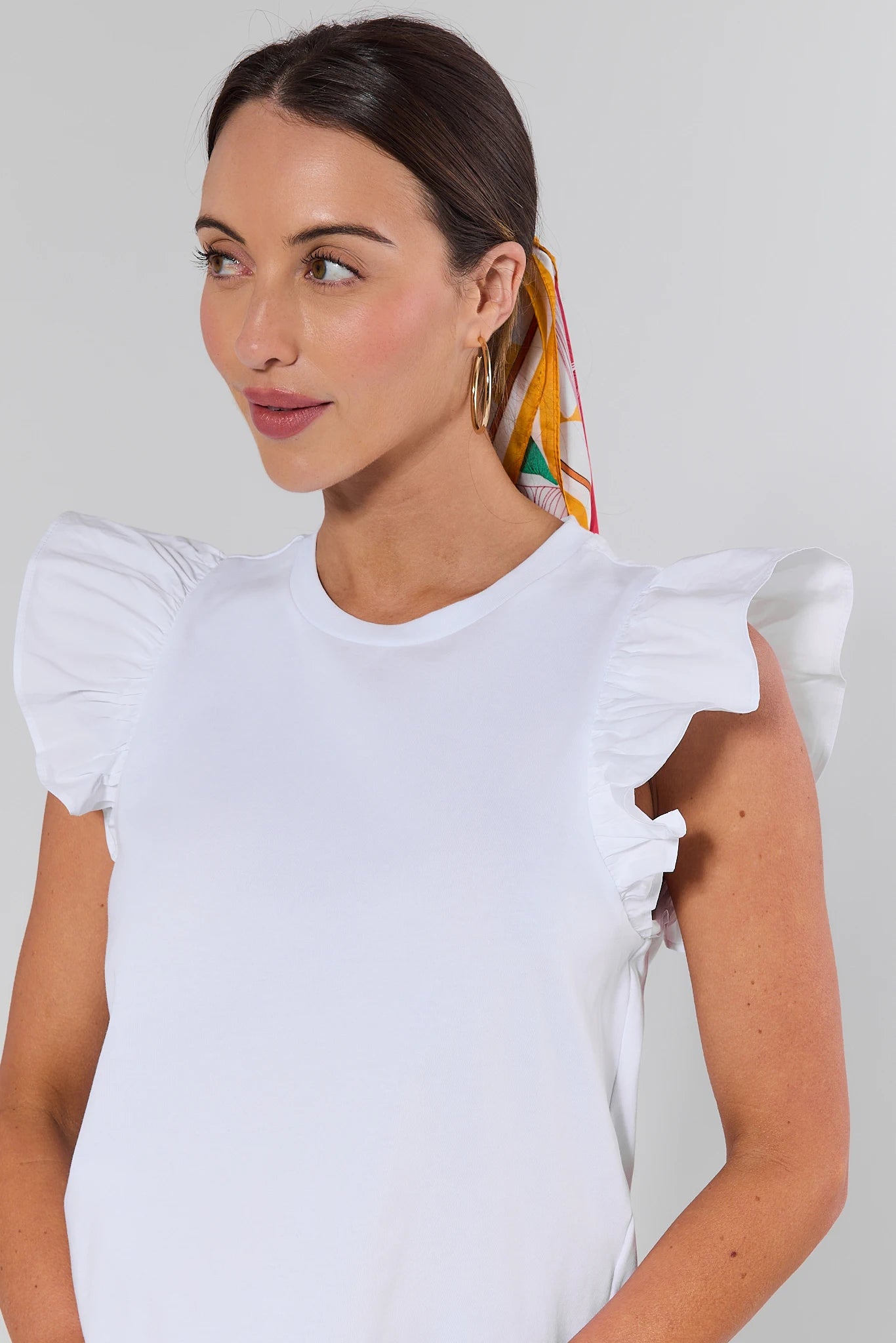 Woman wearing a white top with ruffled sleeves against a plain background