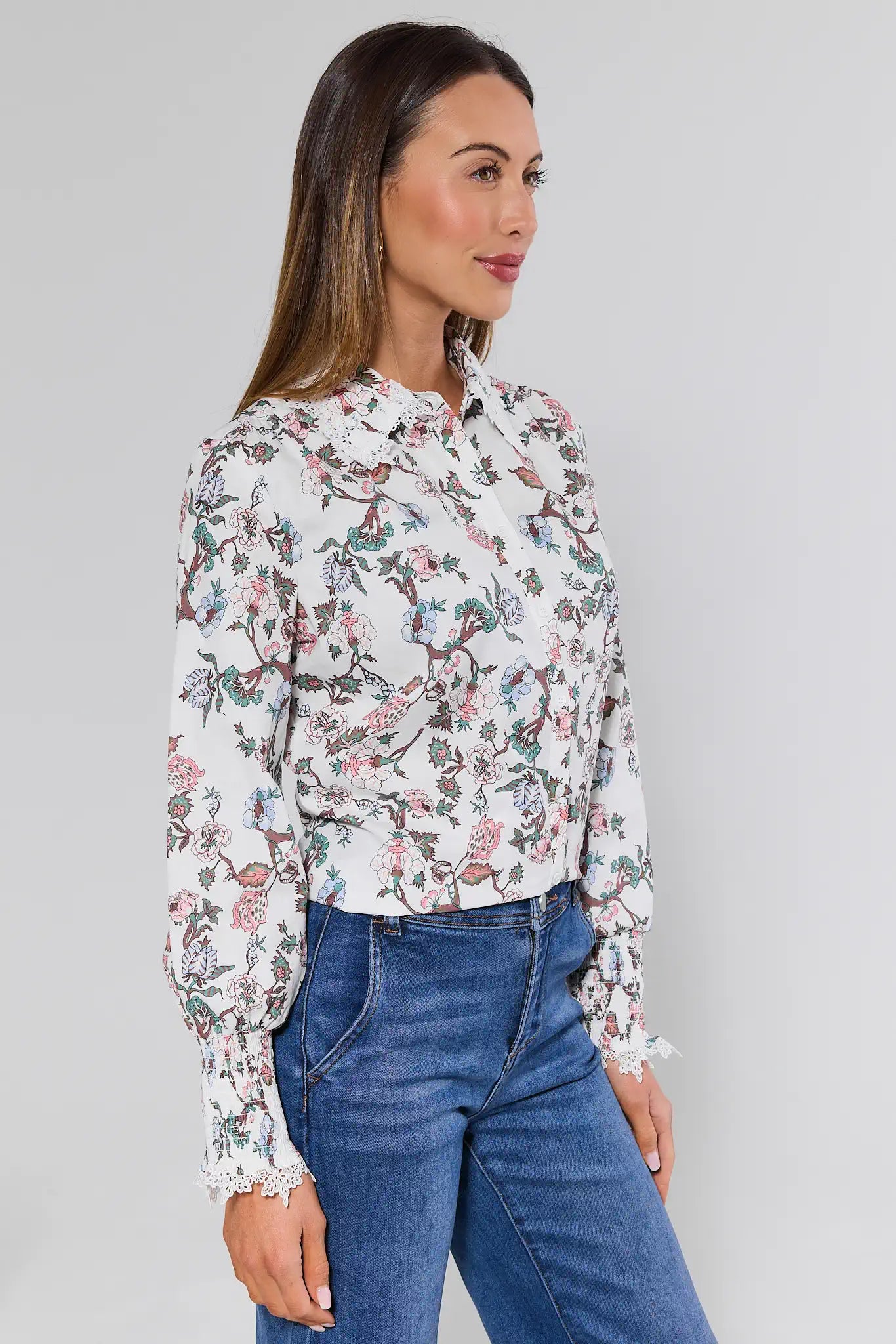 Woman wearing a floral blouse and blue jeans against a plain background