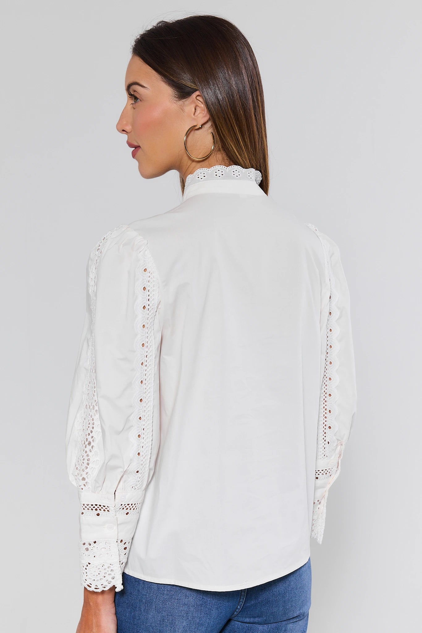 Woman wearing a white blouse with lace details on a plain background