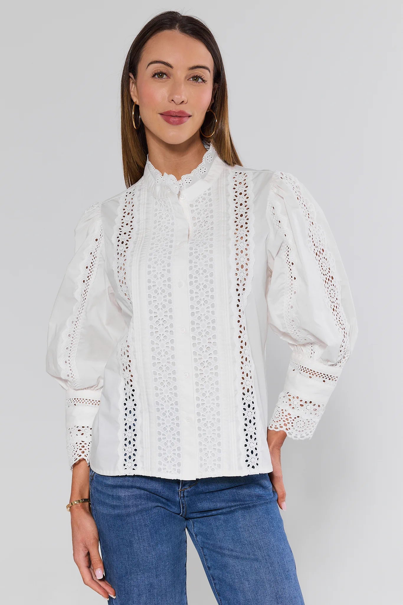 Woman wearing a white blouse with lace details and blue jeans on a plain background