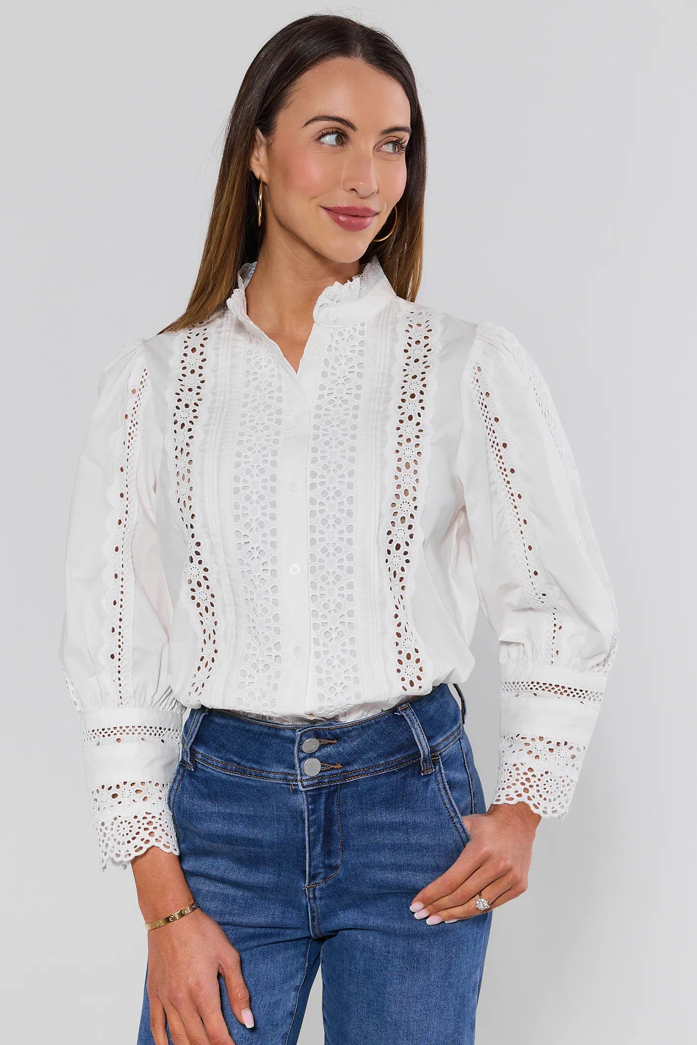 Woman wearing a white blouse with lace details and blue jeans on a plain background
