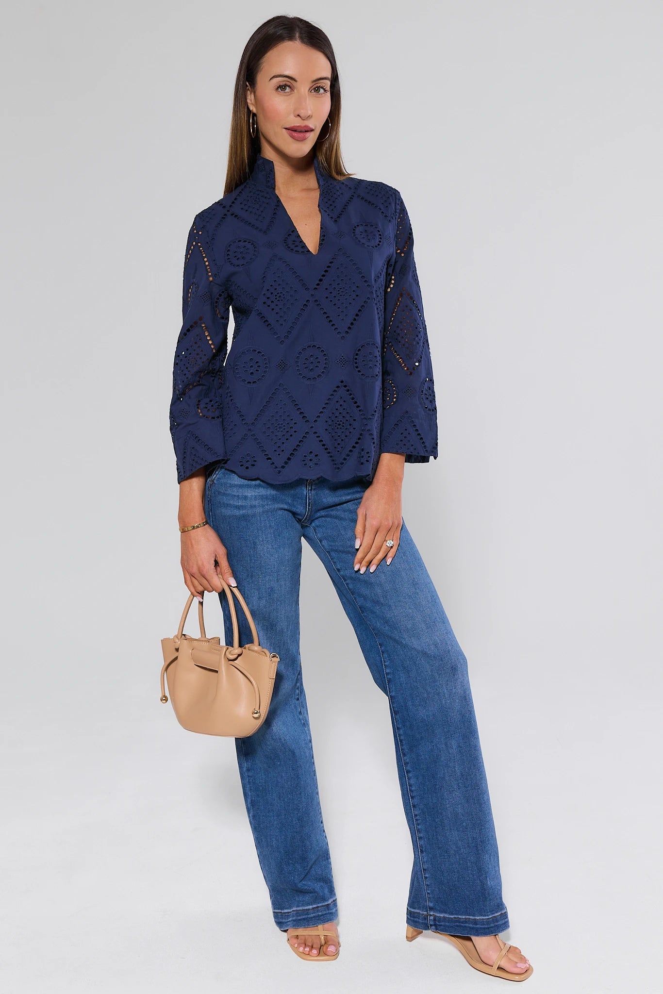 Woman wearing a navy blue patterned jacket and jeans, holding a beige handbag on a white background