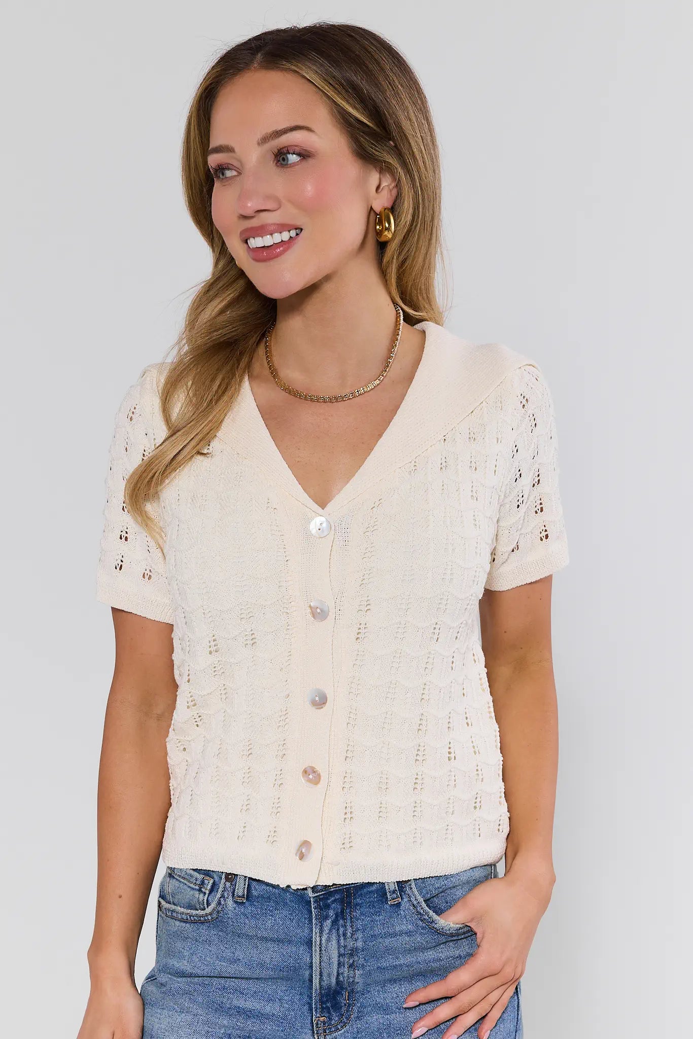 Woman wearing a cream-colored knit cardigan with button details on a plain background