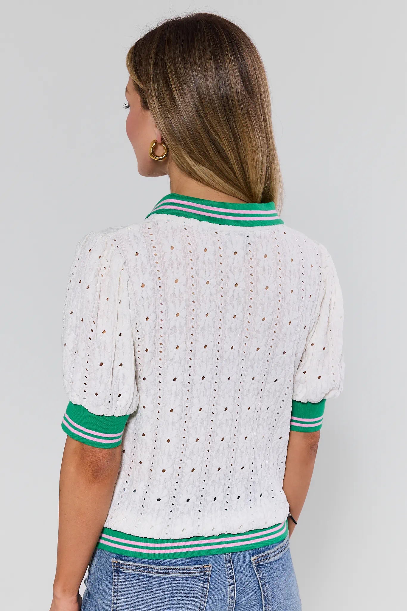 Woman wearing a white eyelet top with green trim on a plain background