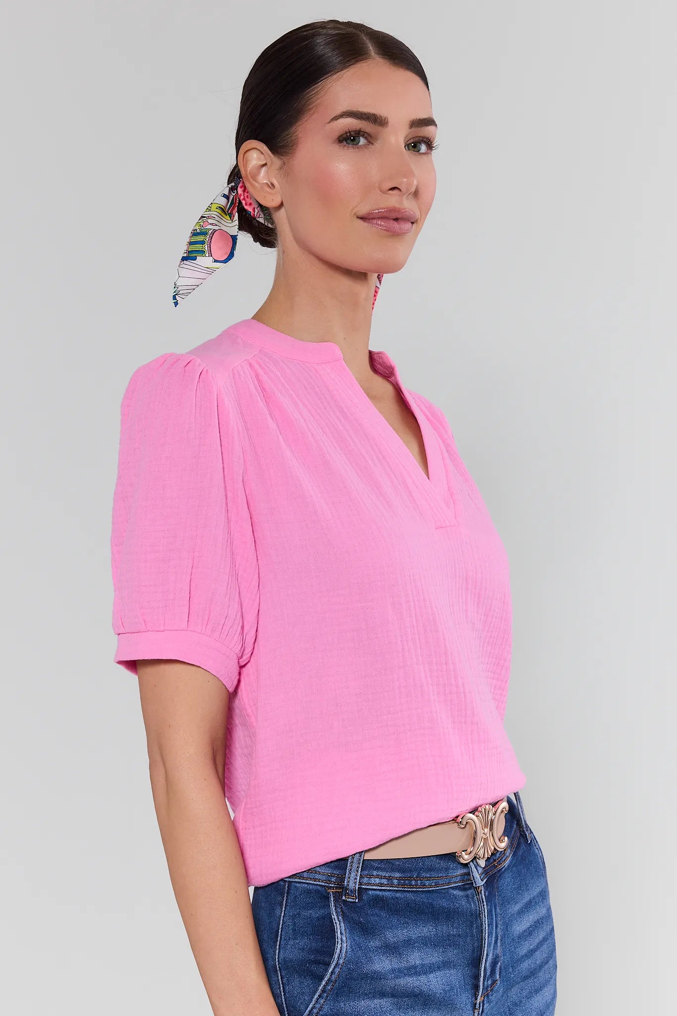 Woman wearing a pink blouse and blue jeans against a plain background