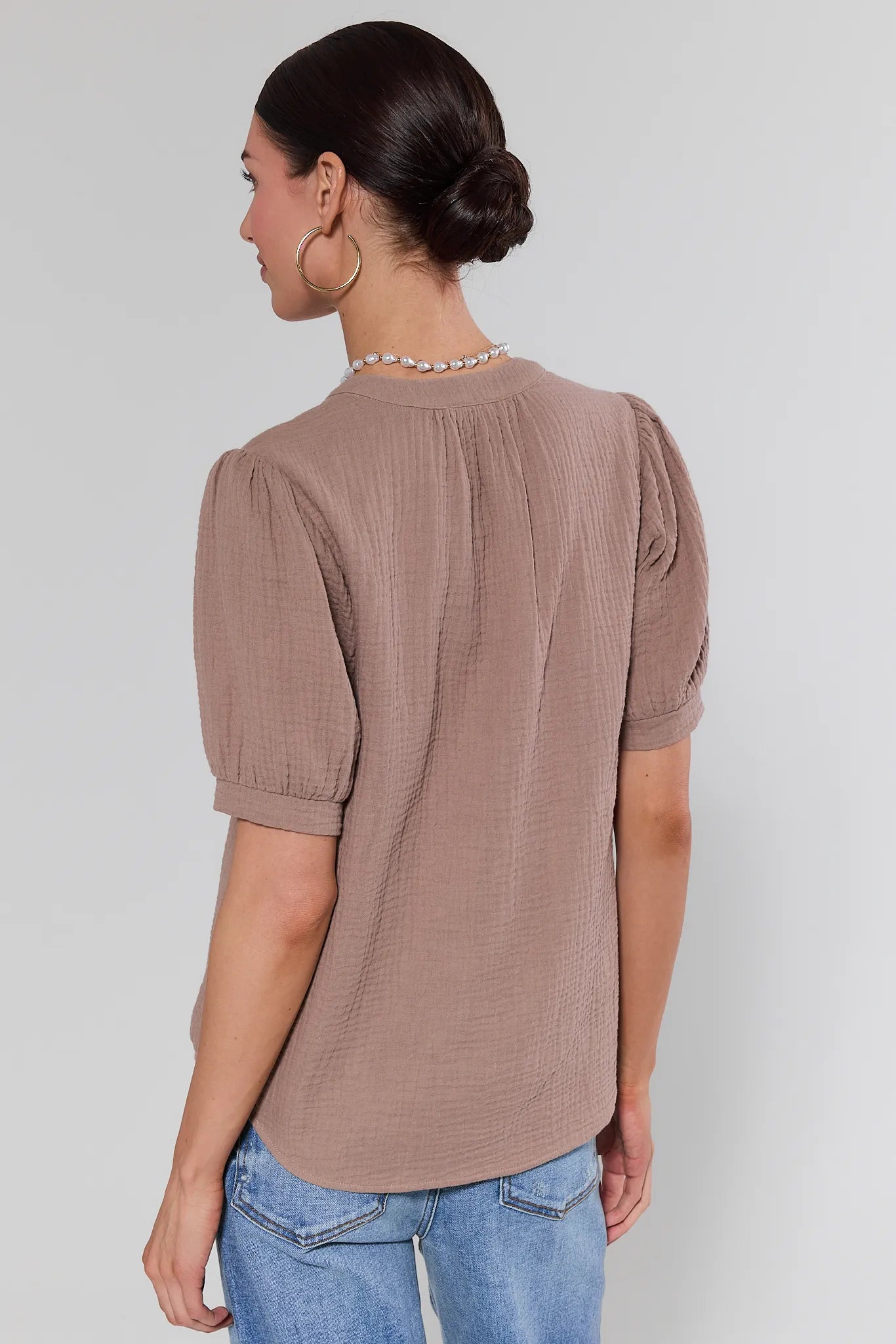 Woman wearing a brown textured blouse and blue jeans against a plain background