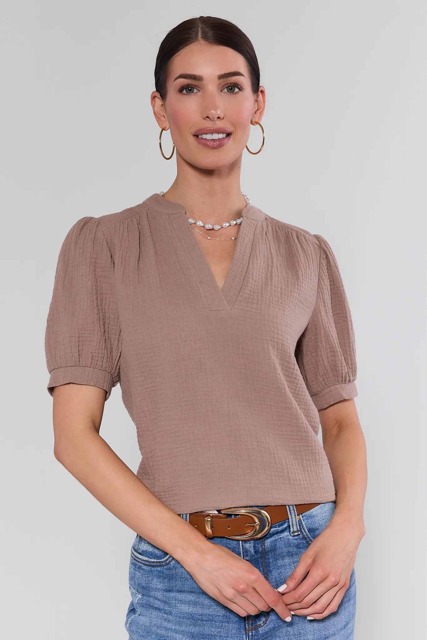 Woman wearing a brown textured top and blue jeans on a plain background