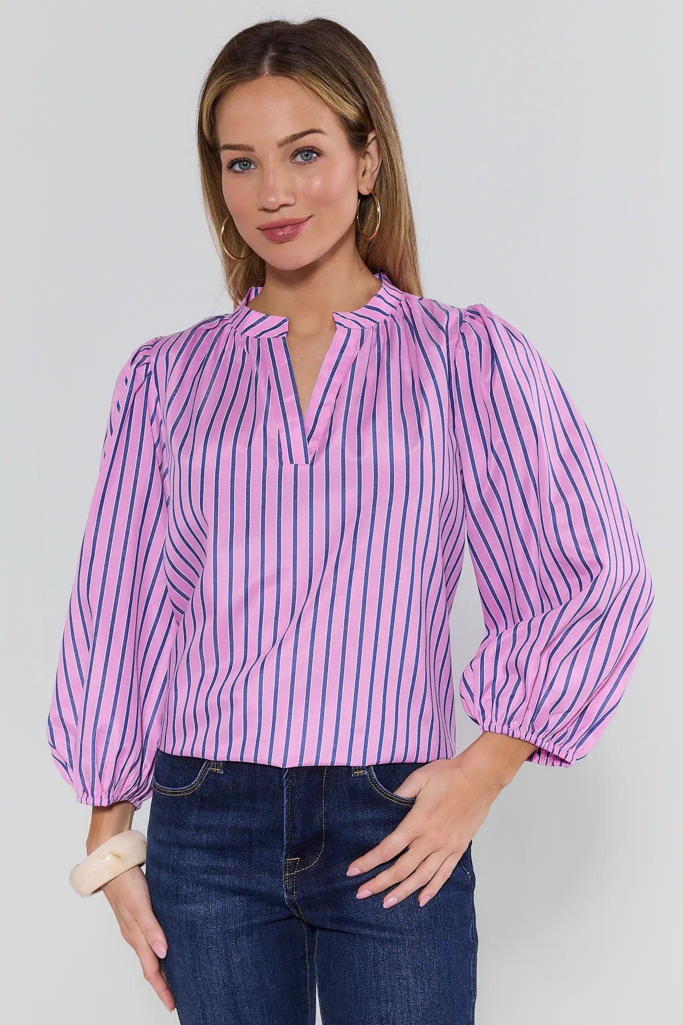 Woman wearing a pink and white striped blouse with blue jeans on a plain background