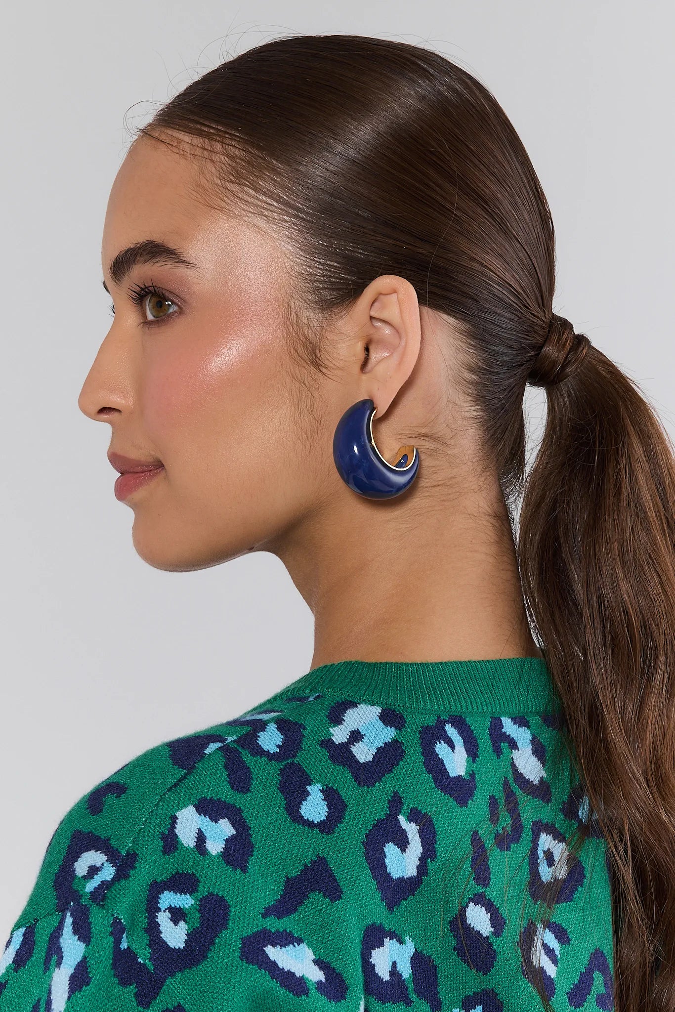 Woman wearing a Tristan Blue Marble Hoop Earrings with a green patterned top on a plain background