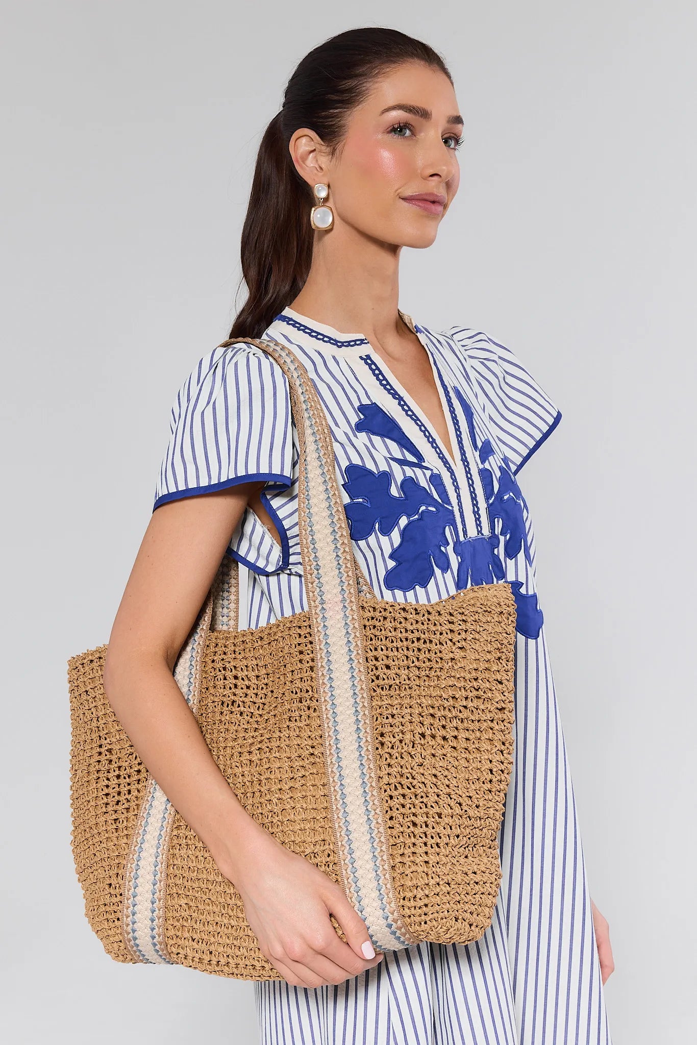 Woman holding a woven tote bag against a plain background