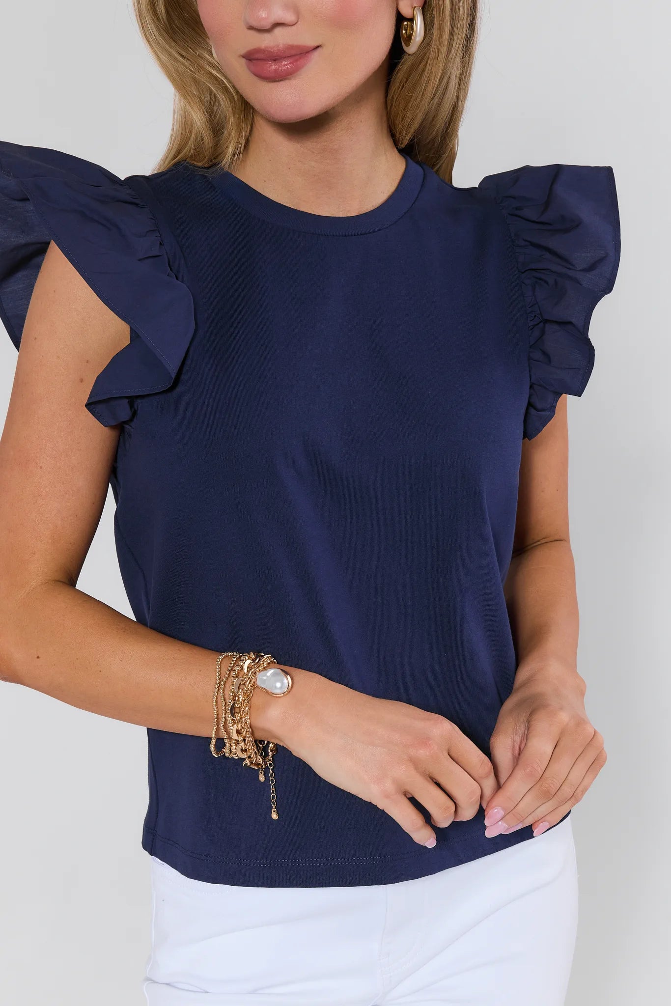 Woman wearing a navy blue top with ruffled sleeves on a plain background