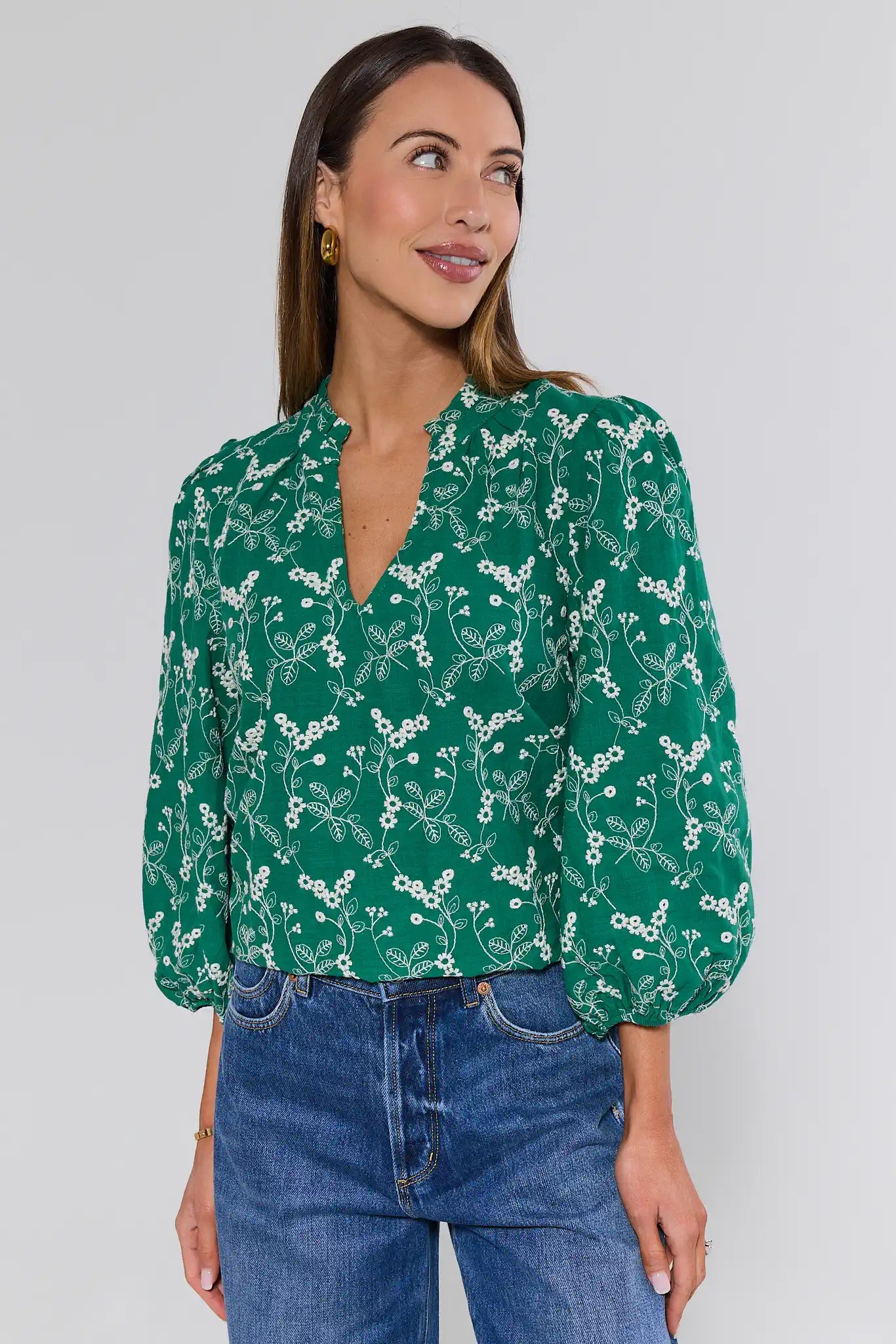 Woman wearing a green floral blouse and blue jeans against a white background