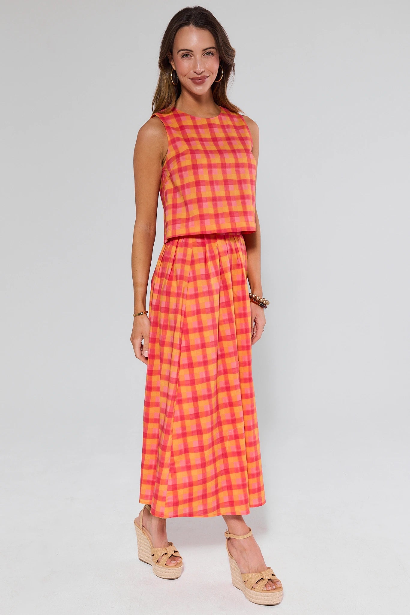 Woman wearing a sleeveless pink and yellow checkered top and matching skirt on a white background