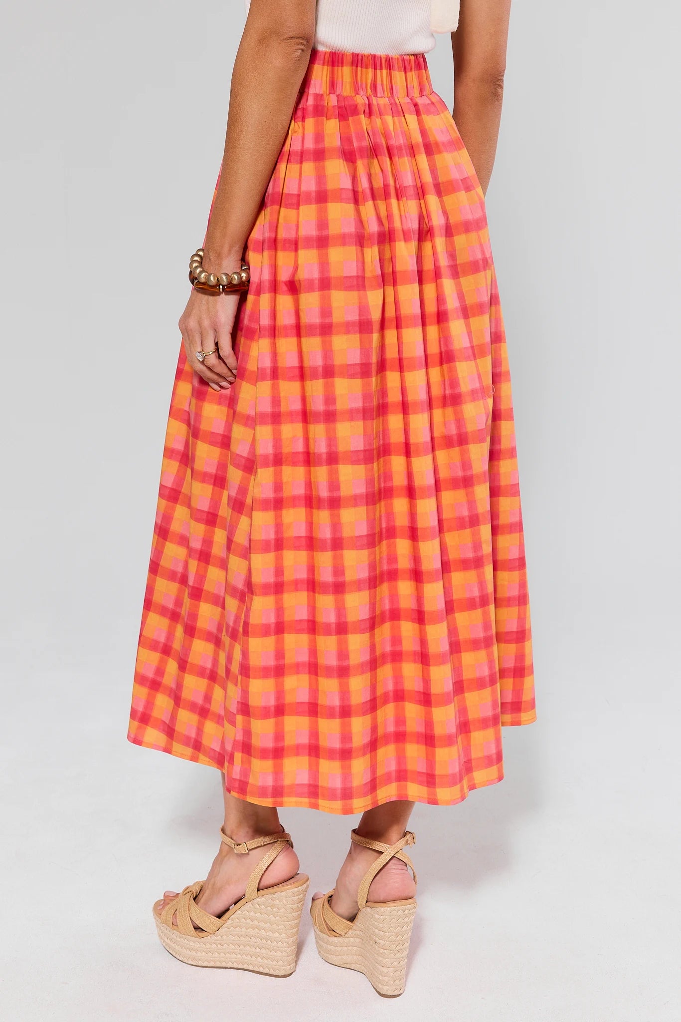 Person wearing a bright pink and orange plaid skirt on a plain background