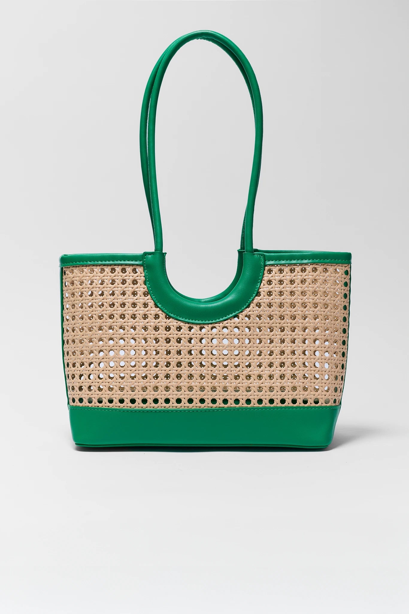 Woven handbag with green handle and base on a light gray background