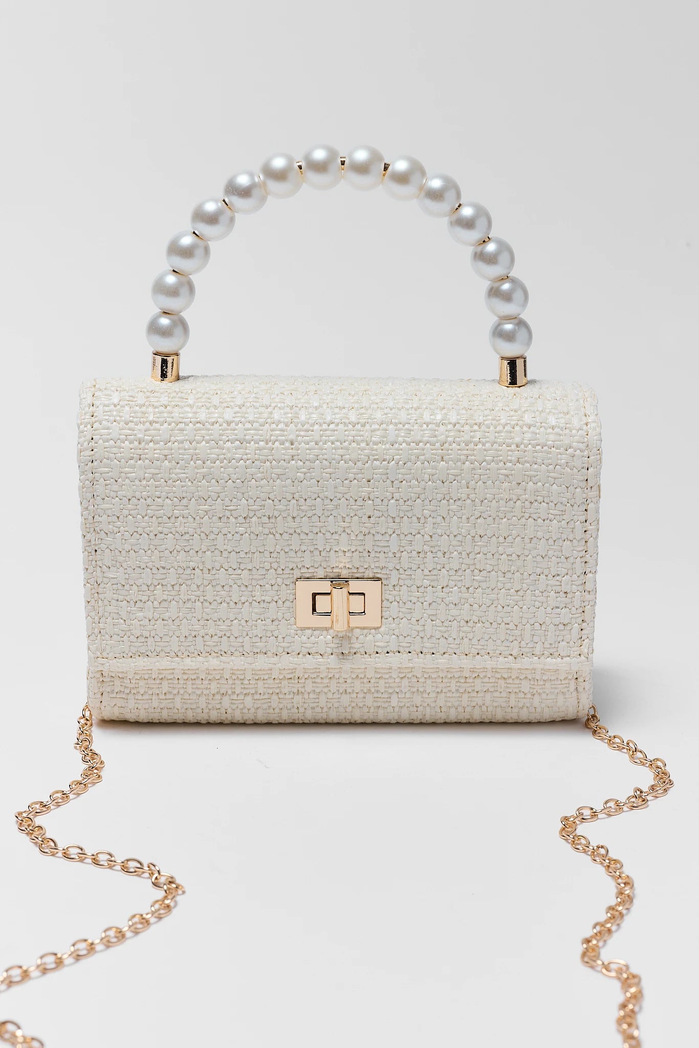 White textured handbag with pearl handle and gold chain on a light gray background