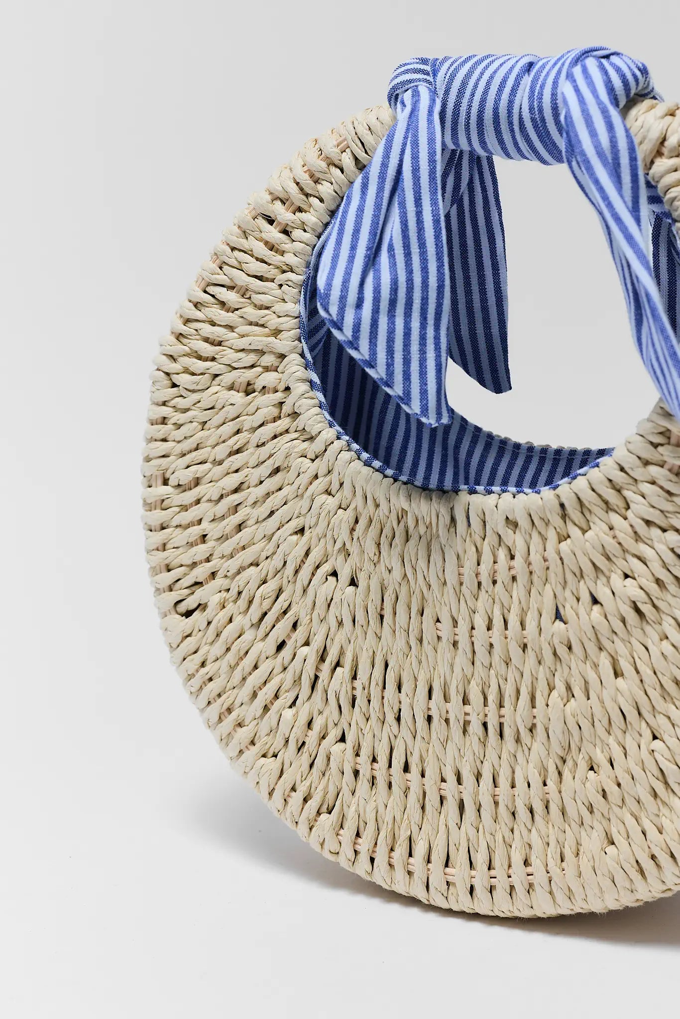 Woven bag with a blue and white striped handle on a light gray background