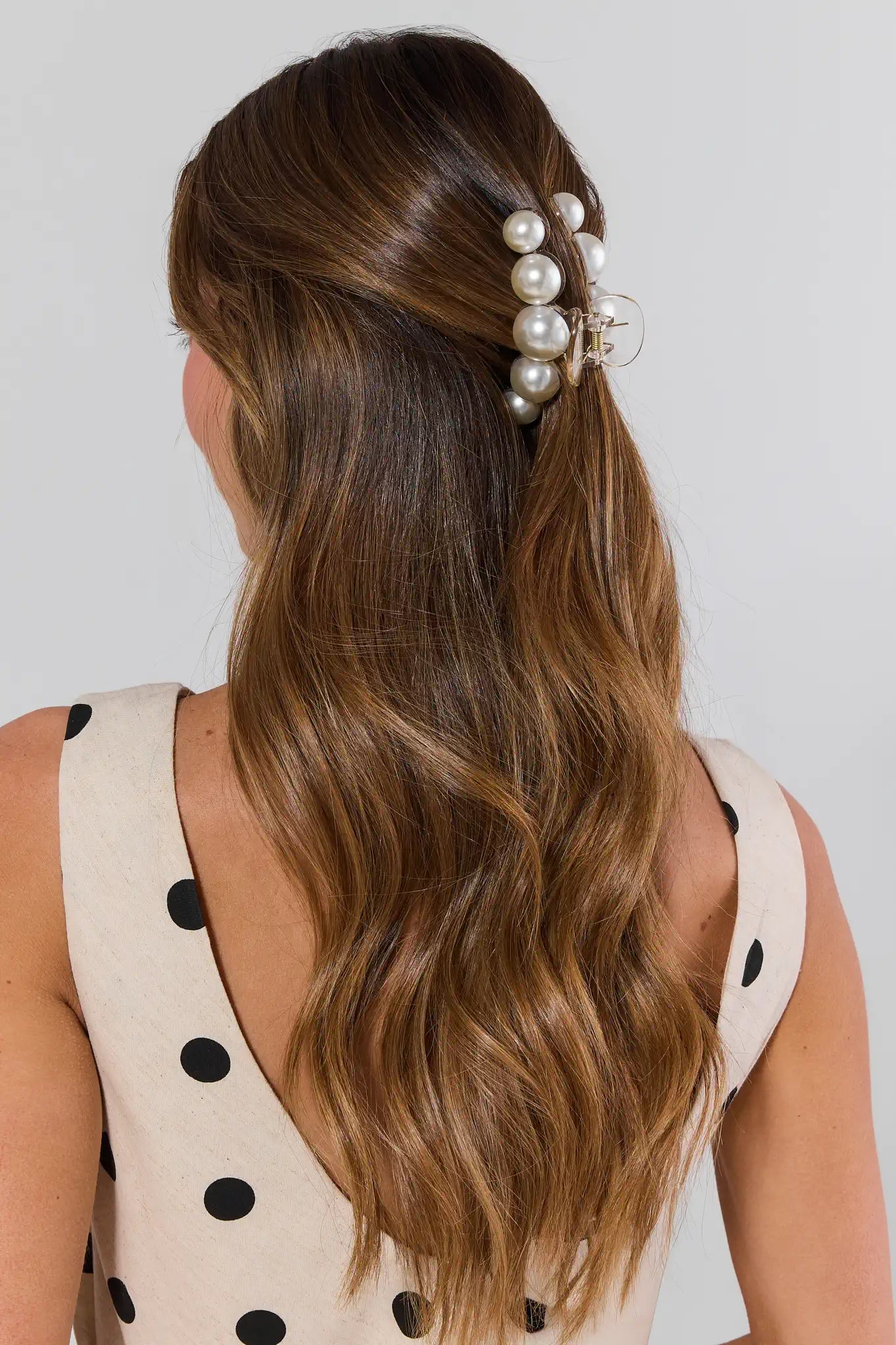 Woman with long brown hair wearing a pearl hair accessory against a plain background