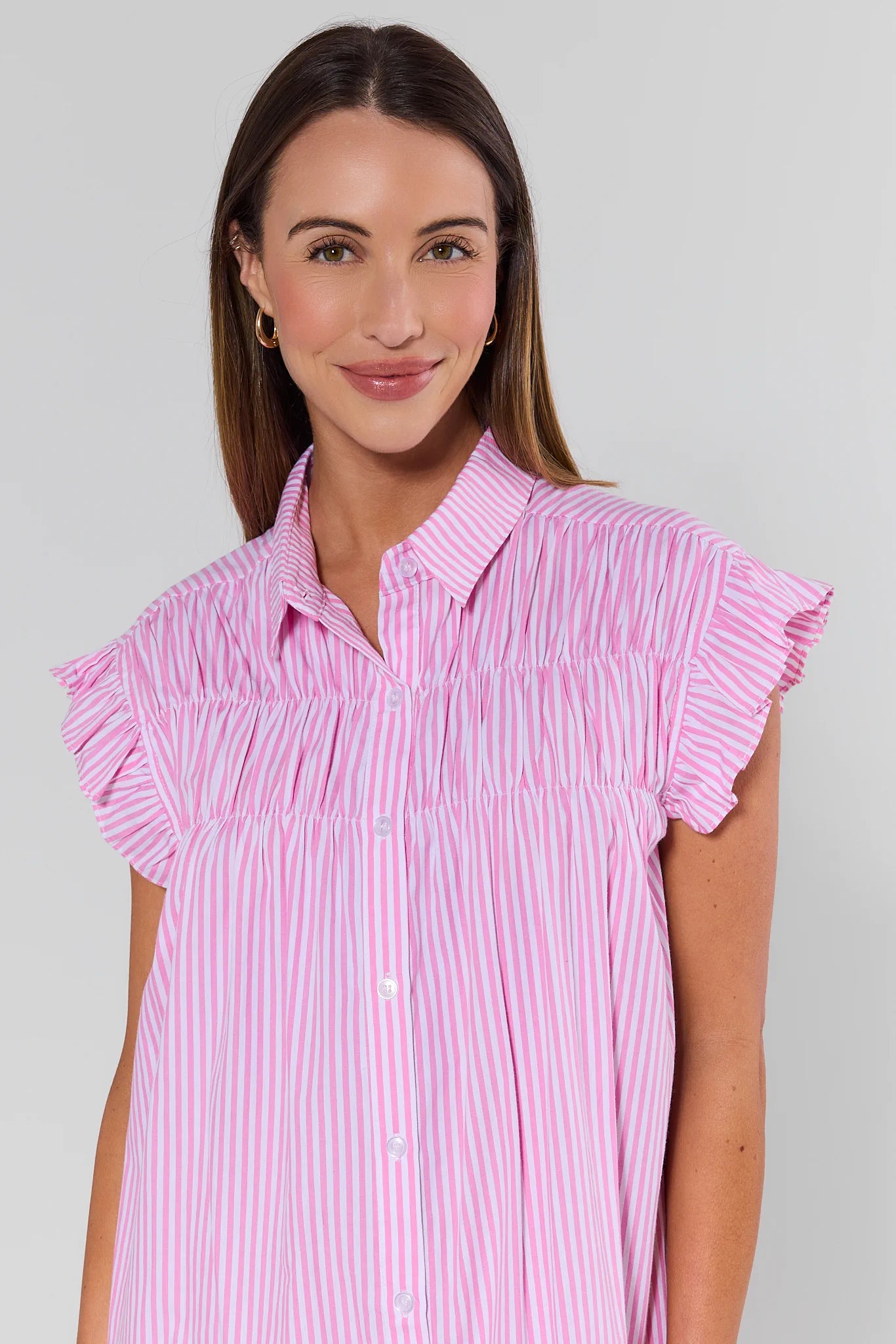 Woman wearing a pink and white striped shirt with ruffled sleeves on a gray background