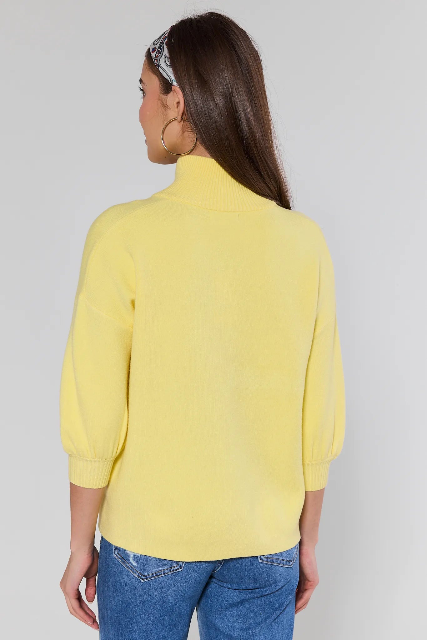 Woman wearing a yellow sweater and blue jeans against a plain background