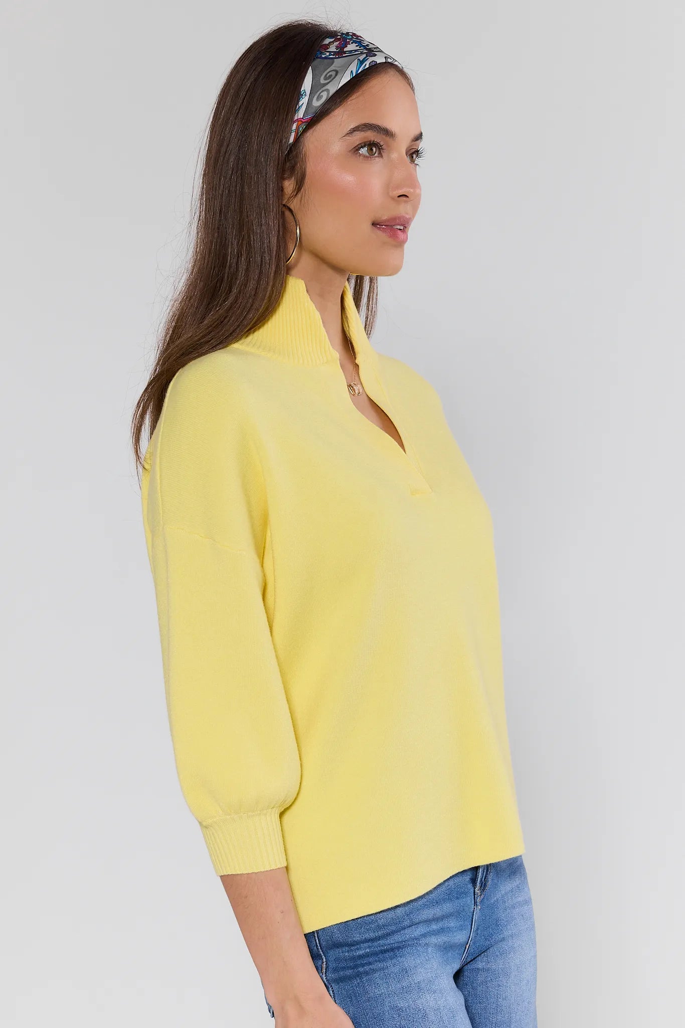 Woman wearing a yellow sweater and blue jeans against a plain background