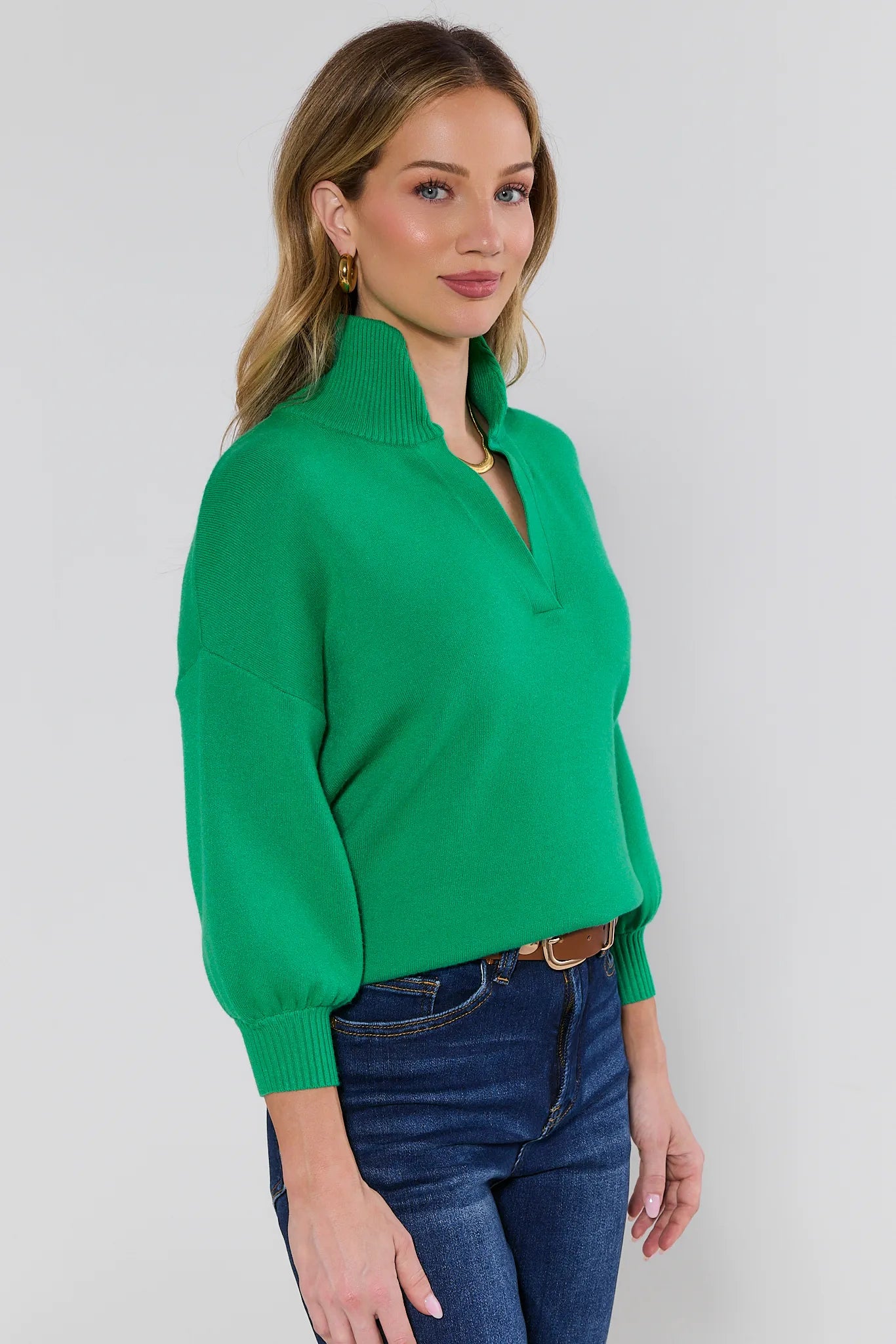 Woman wearing a green sweater and blue jeans against a white background