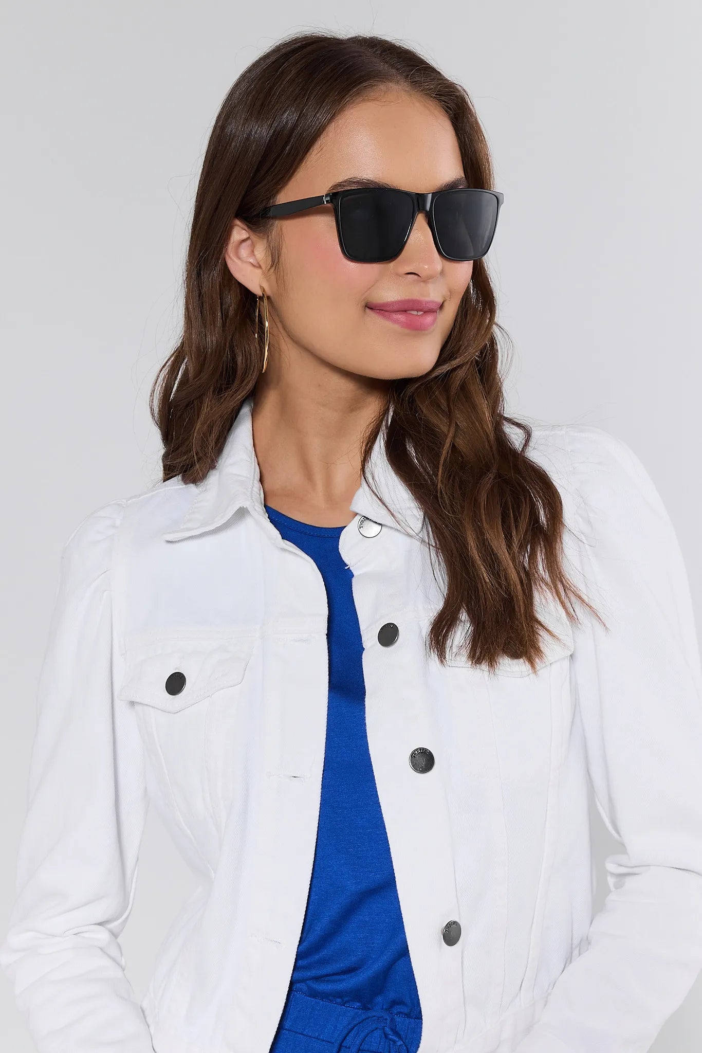 Woman wearing a white jacket and blue shirt with sunglasses against a light gray background