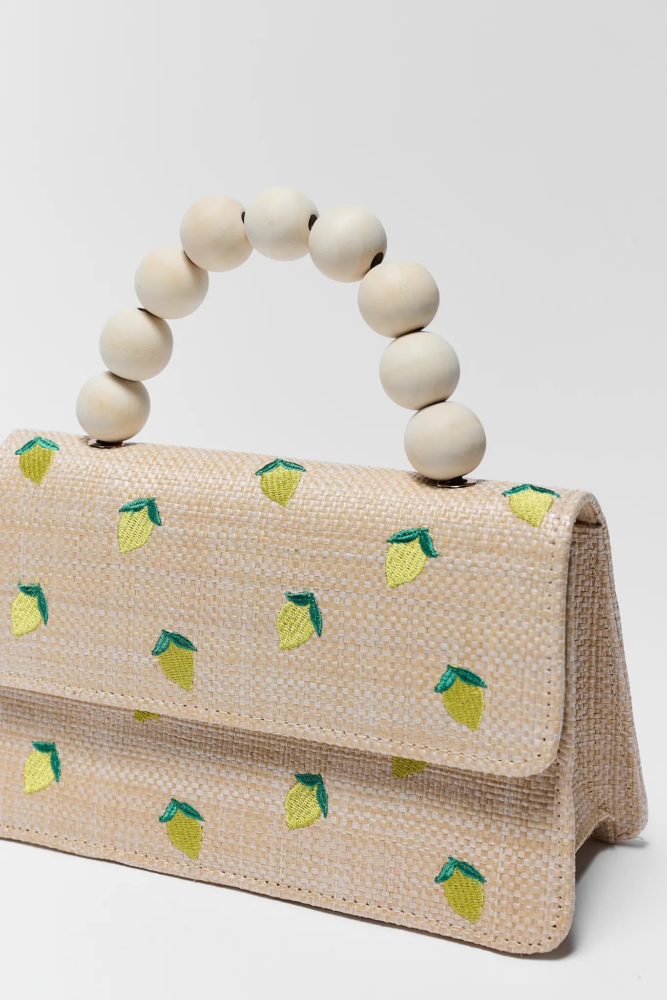 Beige handbag with lemon pattern and wooden bead handle on a white background