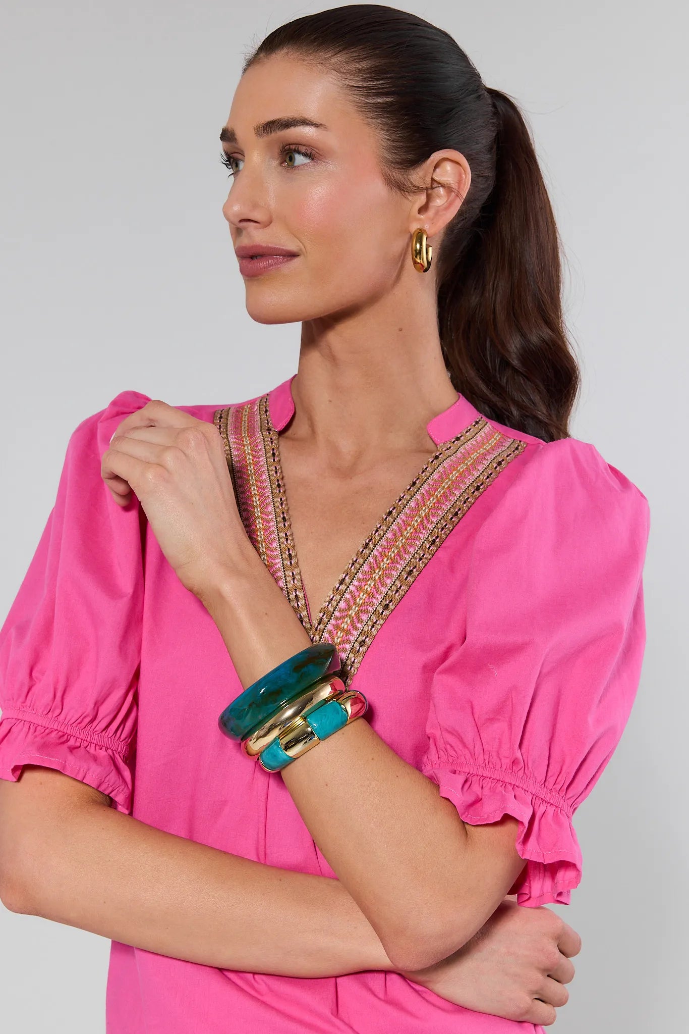 Woman wearing a bright pink blouse with intricate detailing on a plain background