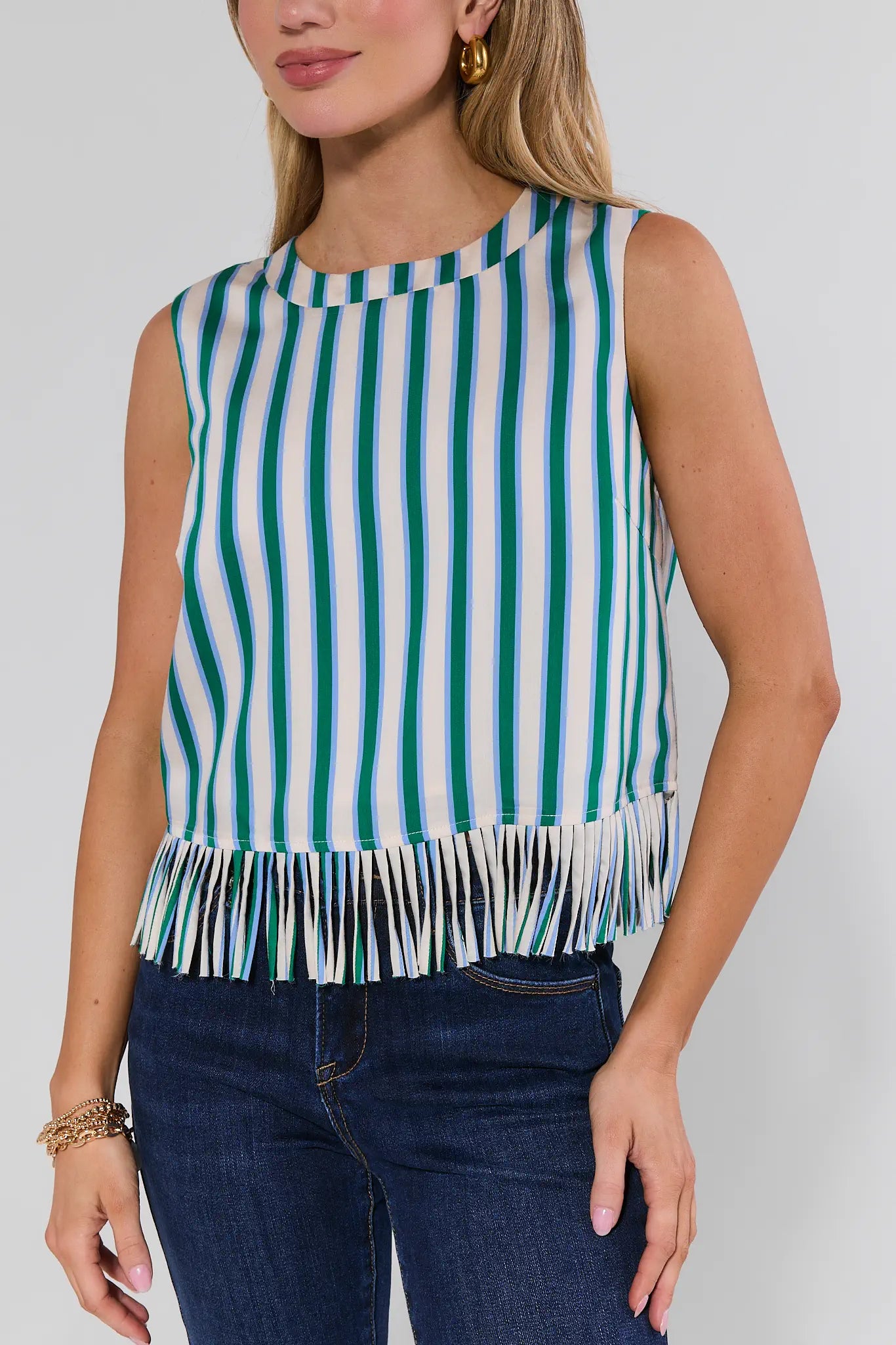Woman wearing a green and white striped sleeveless top with fringe detail on a plain background