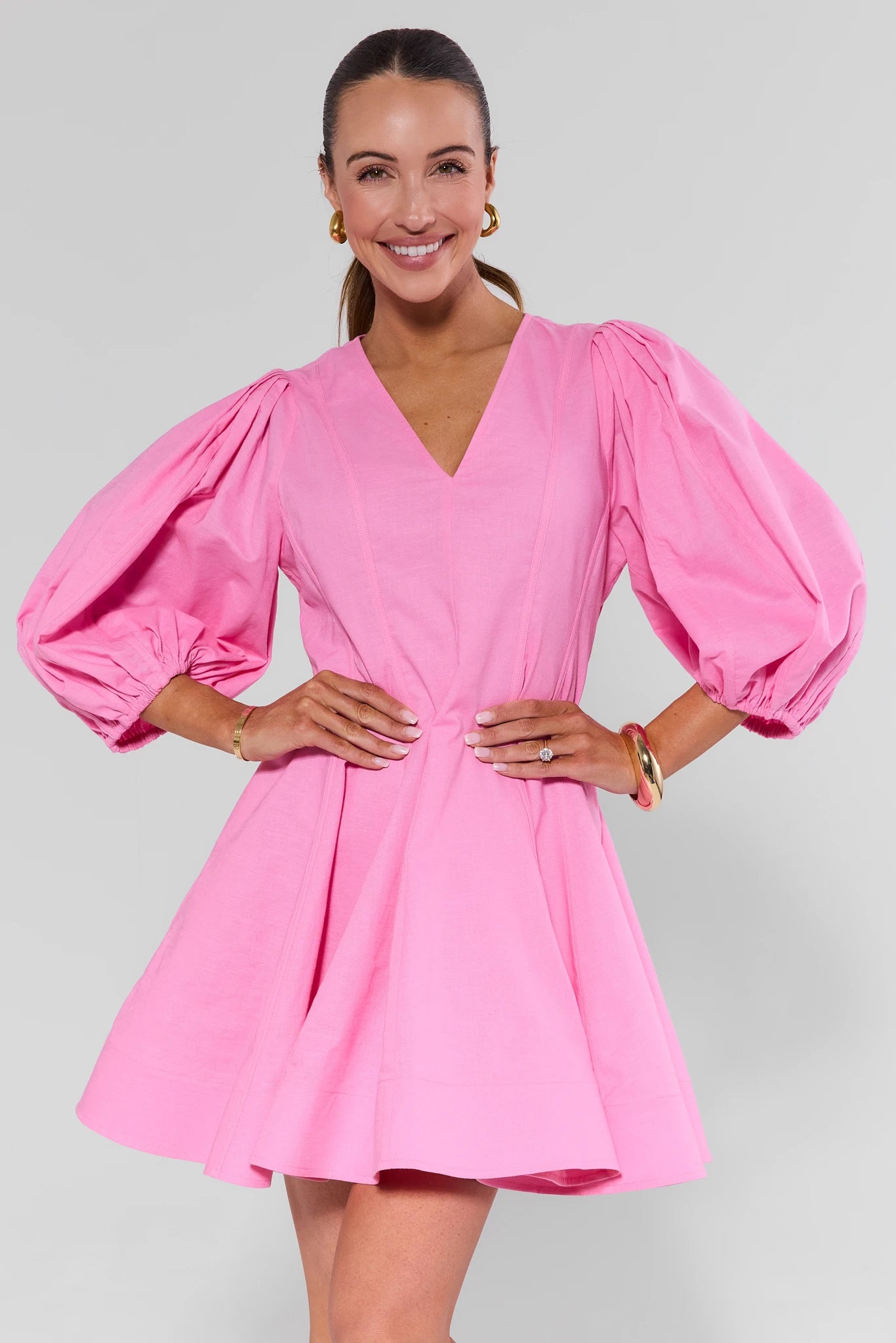 Woman wearing a pink dress with puffed sleeves on a plain background