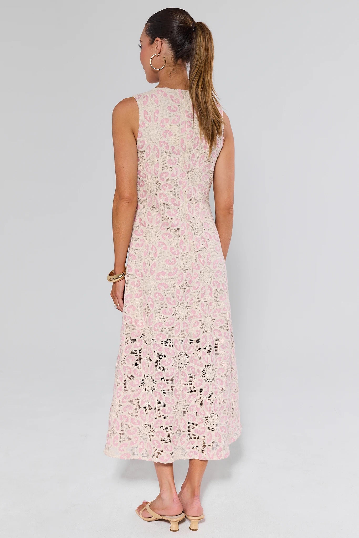 Woman wearing a light pink sleeveless dress with a floral pattern on a plain background