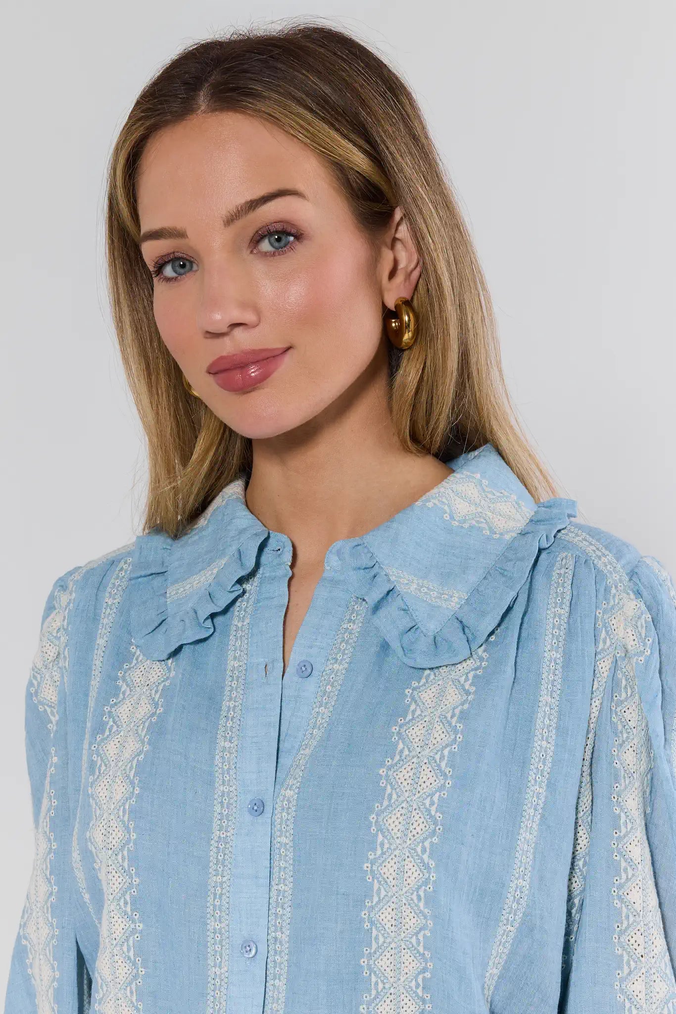 Woman wearing a light blue blouse with lace details against a plain background