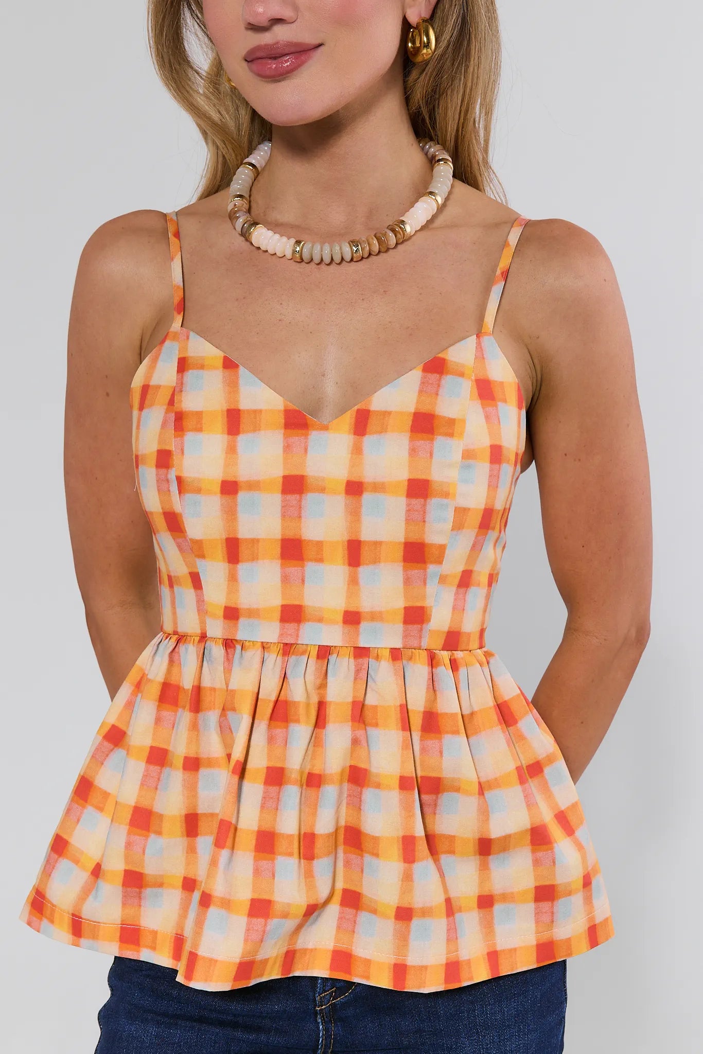 Woman wearing a yellow and orange plaid top against a plain background