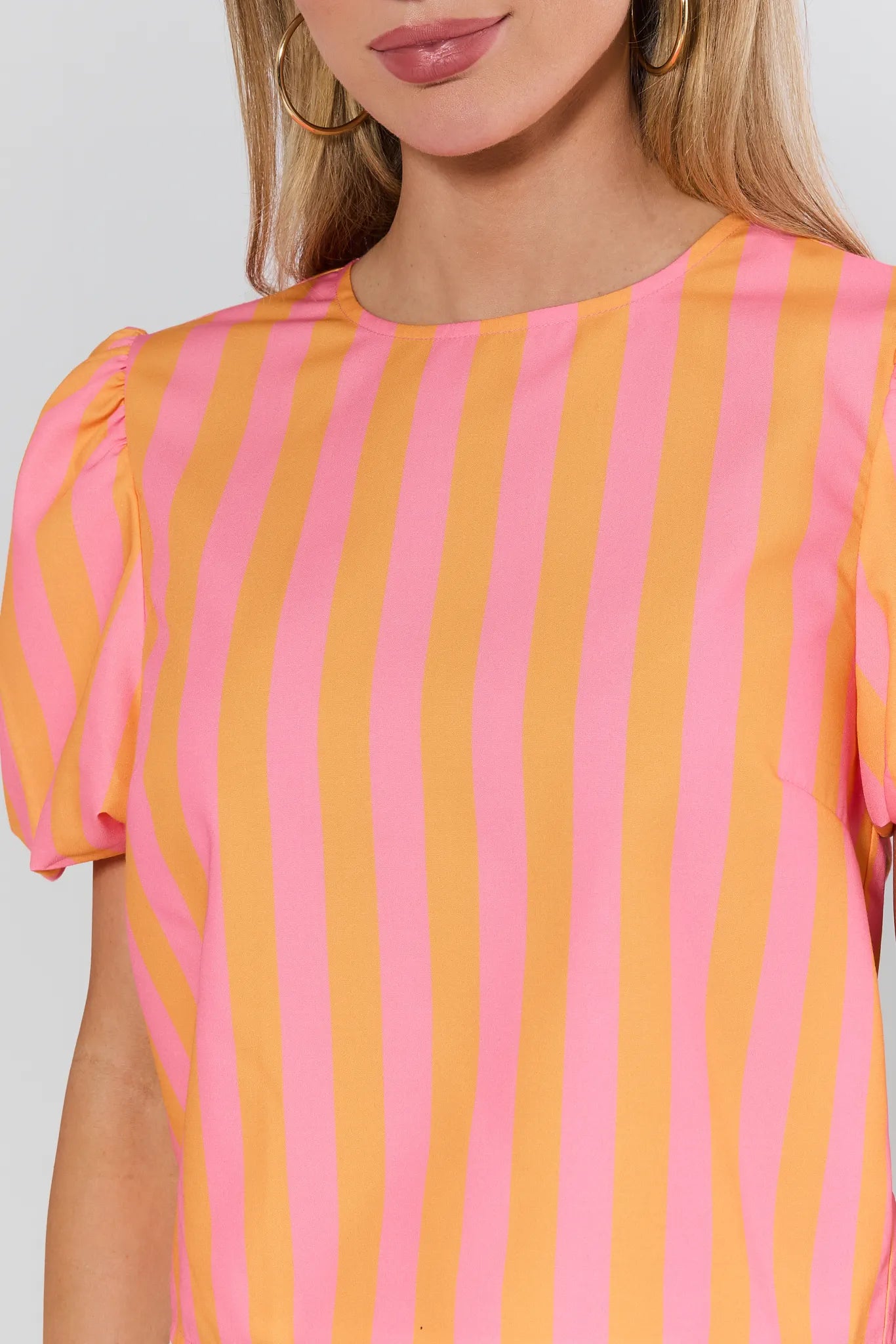 Close-up of a person wearing a pink and orange striped top against a white background