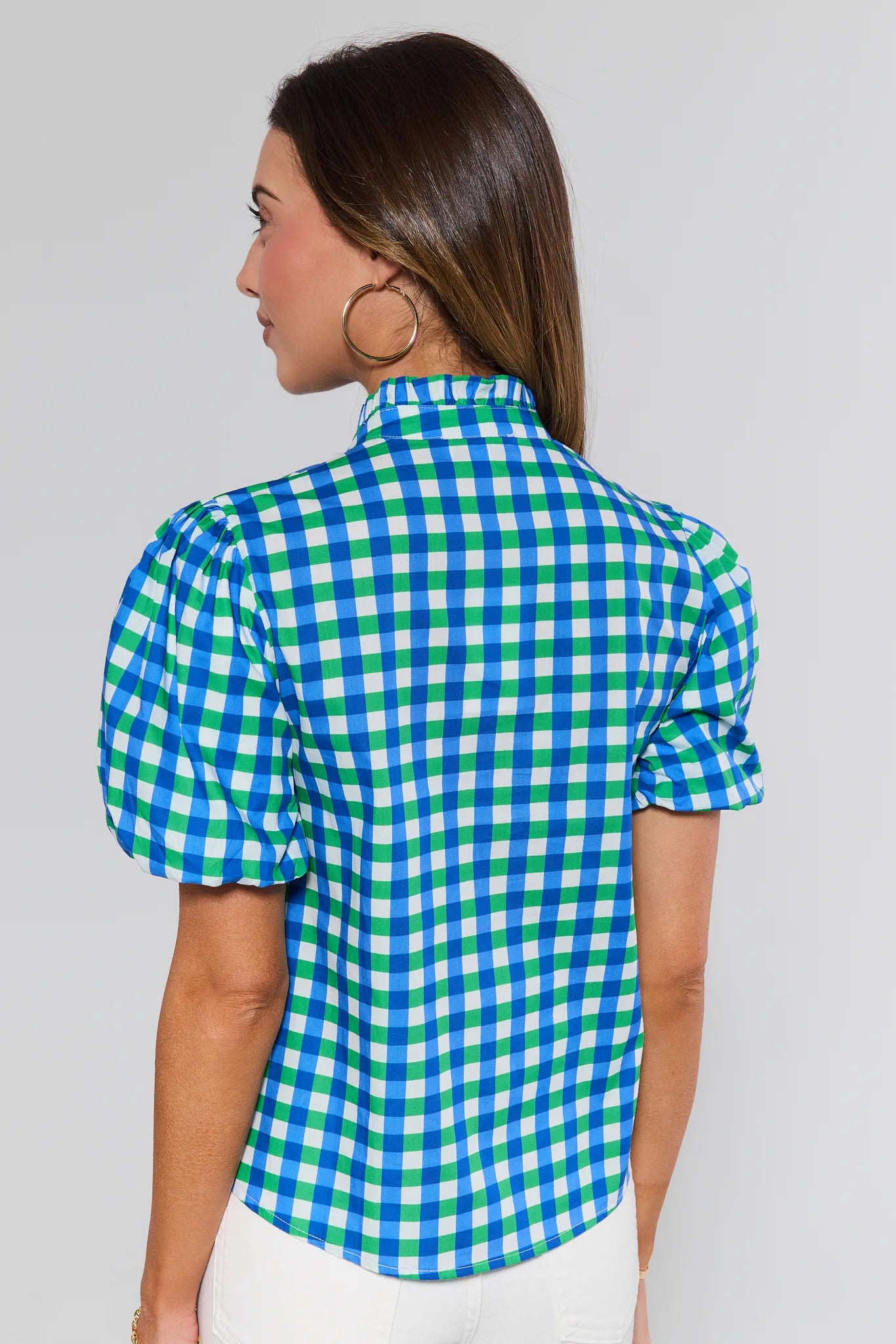 Back view of a woman wearing the Kathleen Mixed Gingham Short Sleeve Top with puff sleeves and hoop earrings, paired with white bottoms.