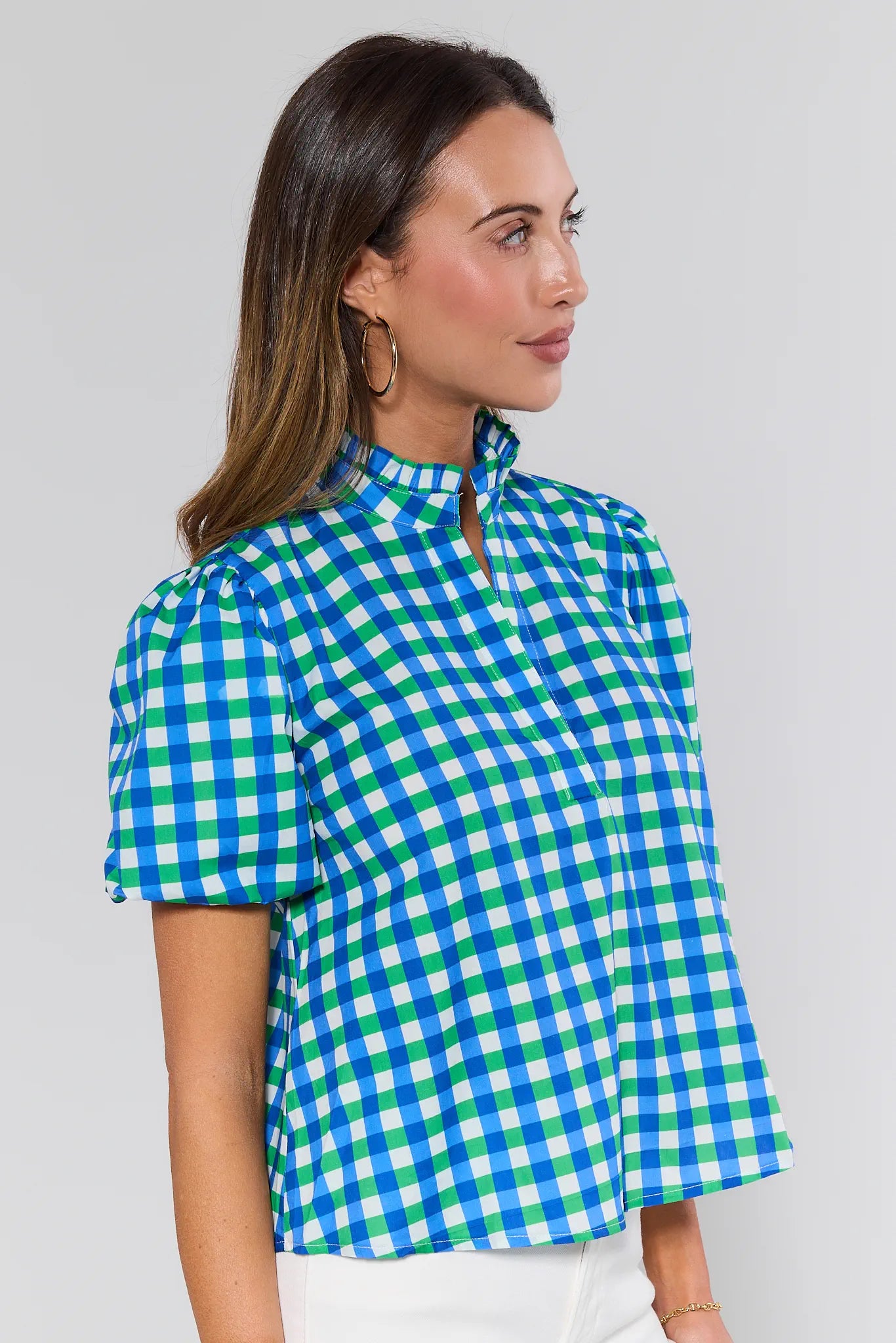 Model wears Kathleen Mixed Gingham Short Sleeve Top with puffed sleeves, ruffled collar, and hidden placket, paired with light bottoms and gold hoop earrings.