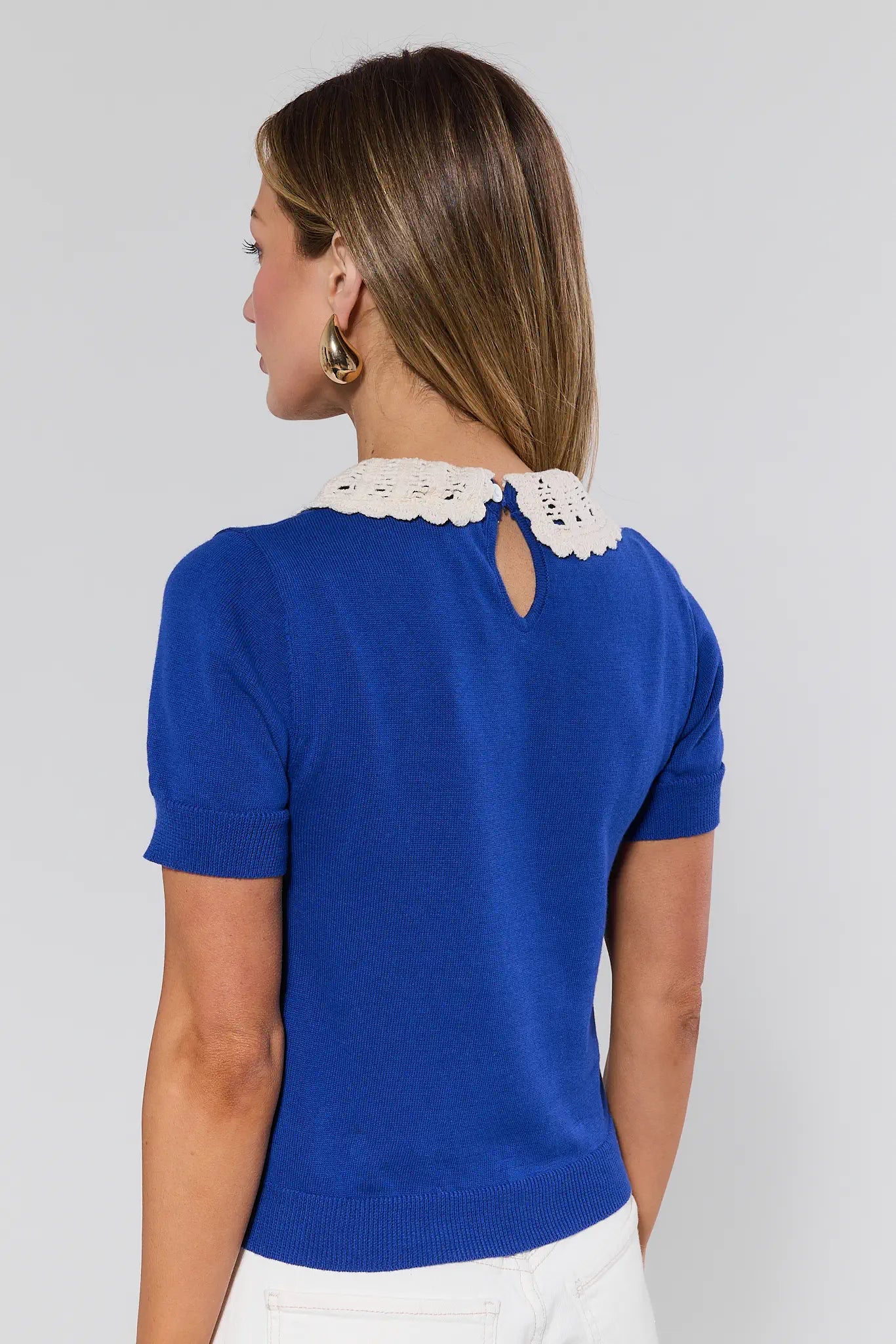 Woman wearing a blue top with a white lace collar on a plain background