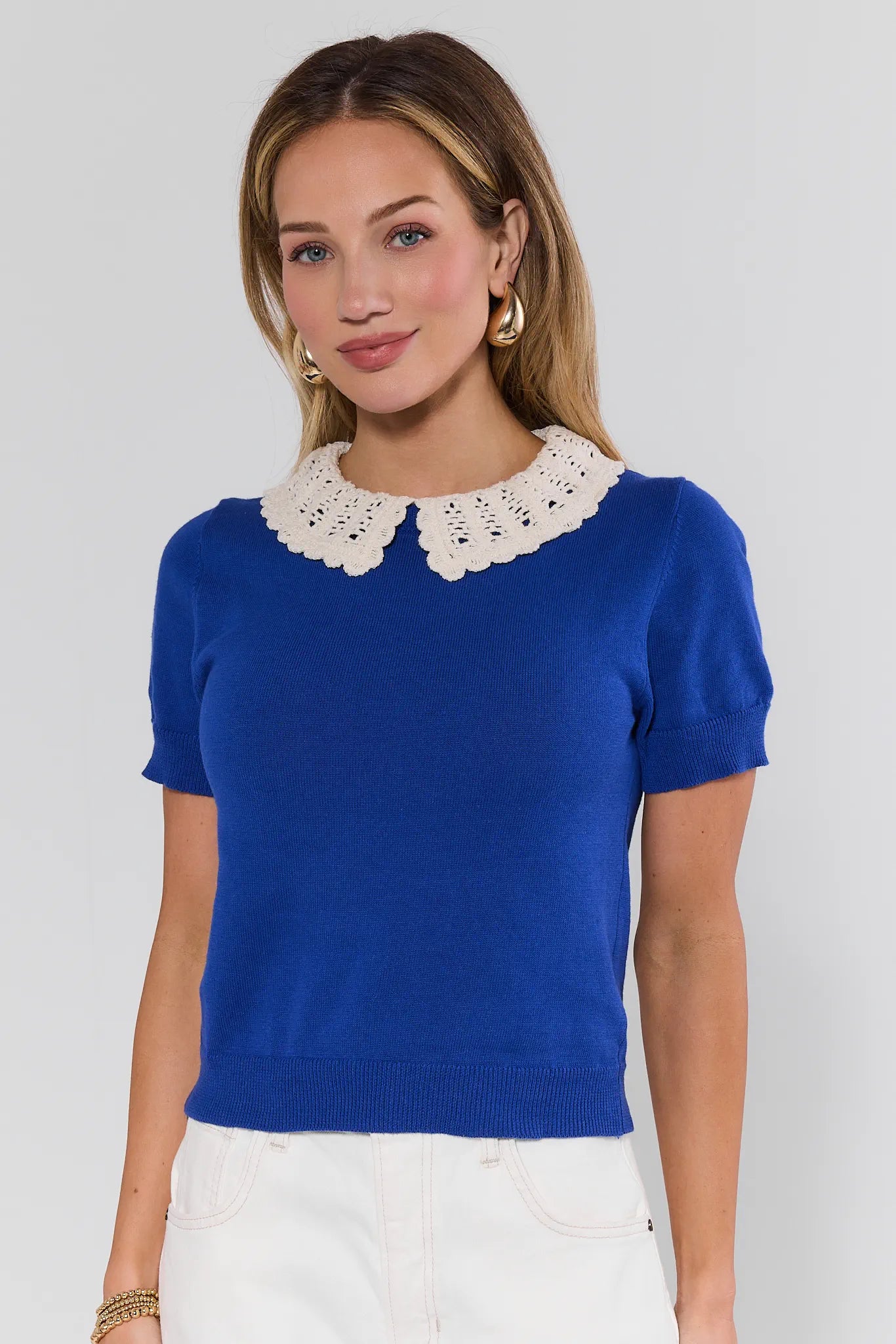 Woman wearing a blue top with a white lace collar against a plain background