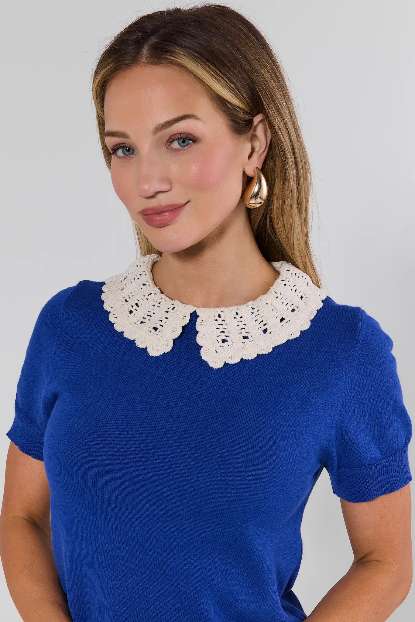 Woman wearing a blue top with a white lace collar against a plain background