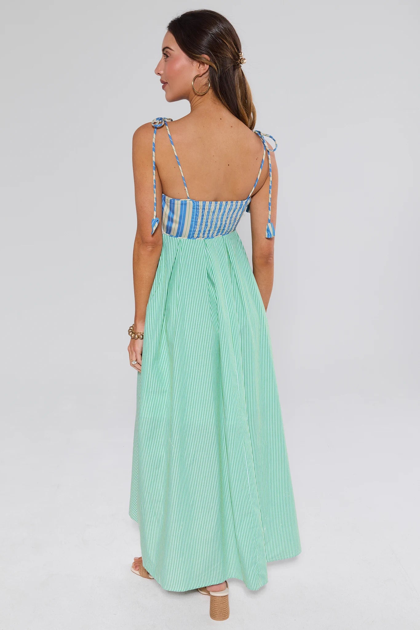 Woman wearing a mint green dress with blue and white striped top on a light gray background