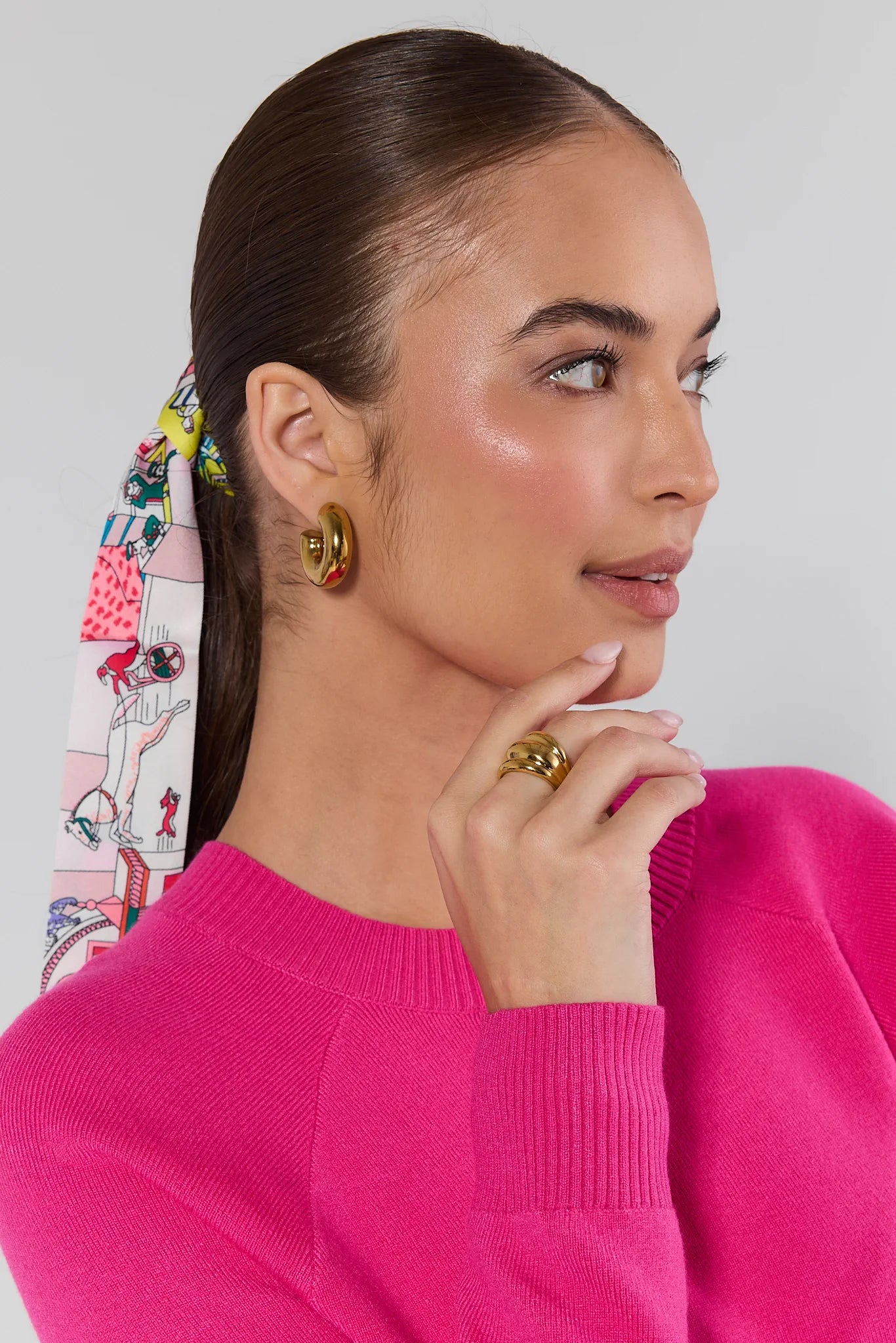 Woman wearing a bright pink sweater with gold earrings and Daley Gold Fluted Ring, against a light gray background.