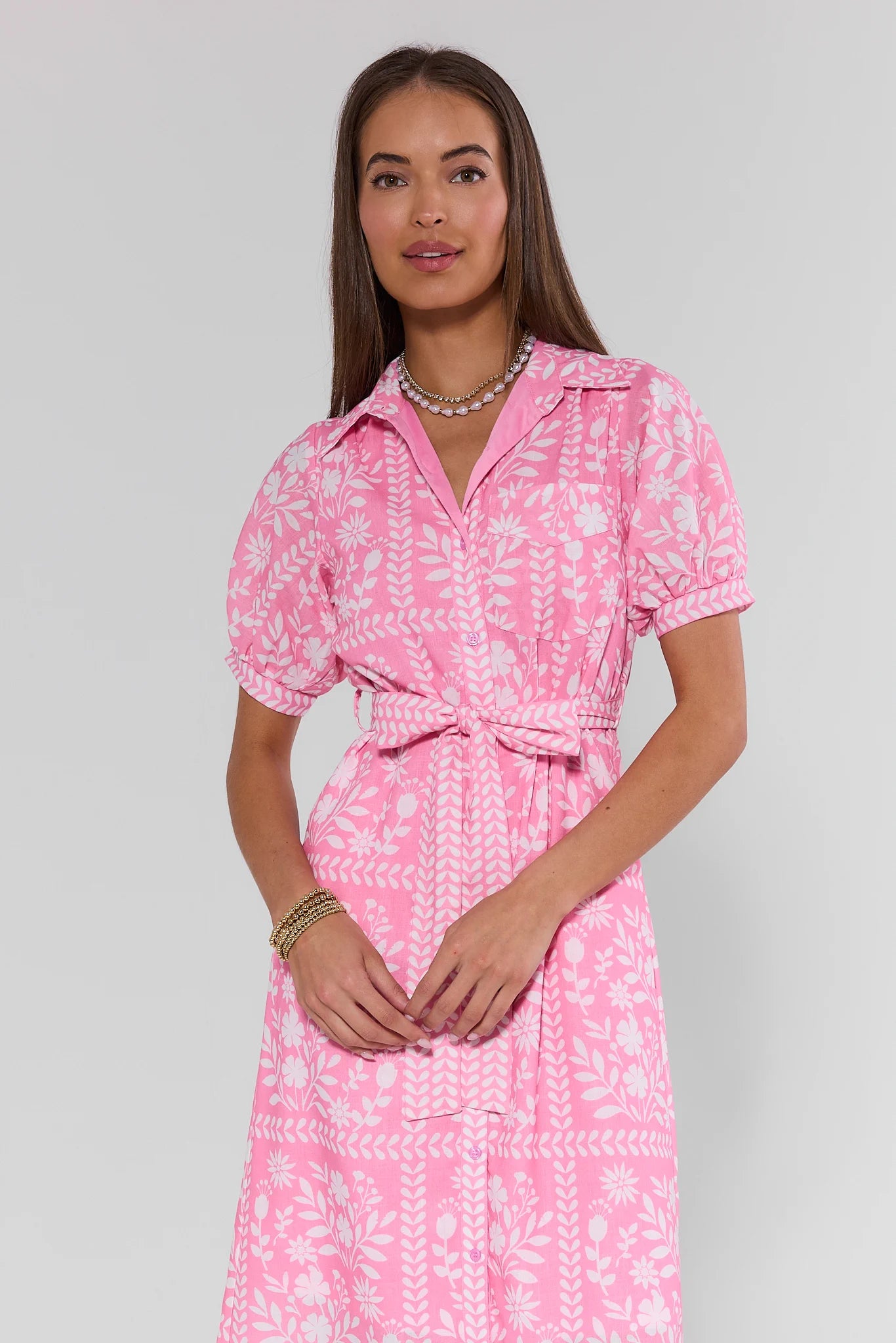 Woman wearing a pink dress with a white pattern on a plain background