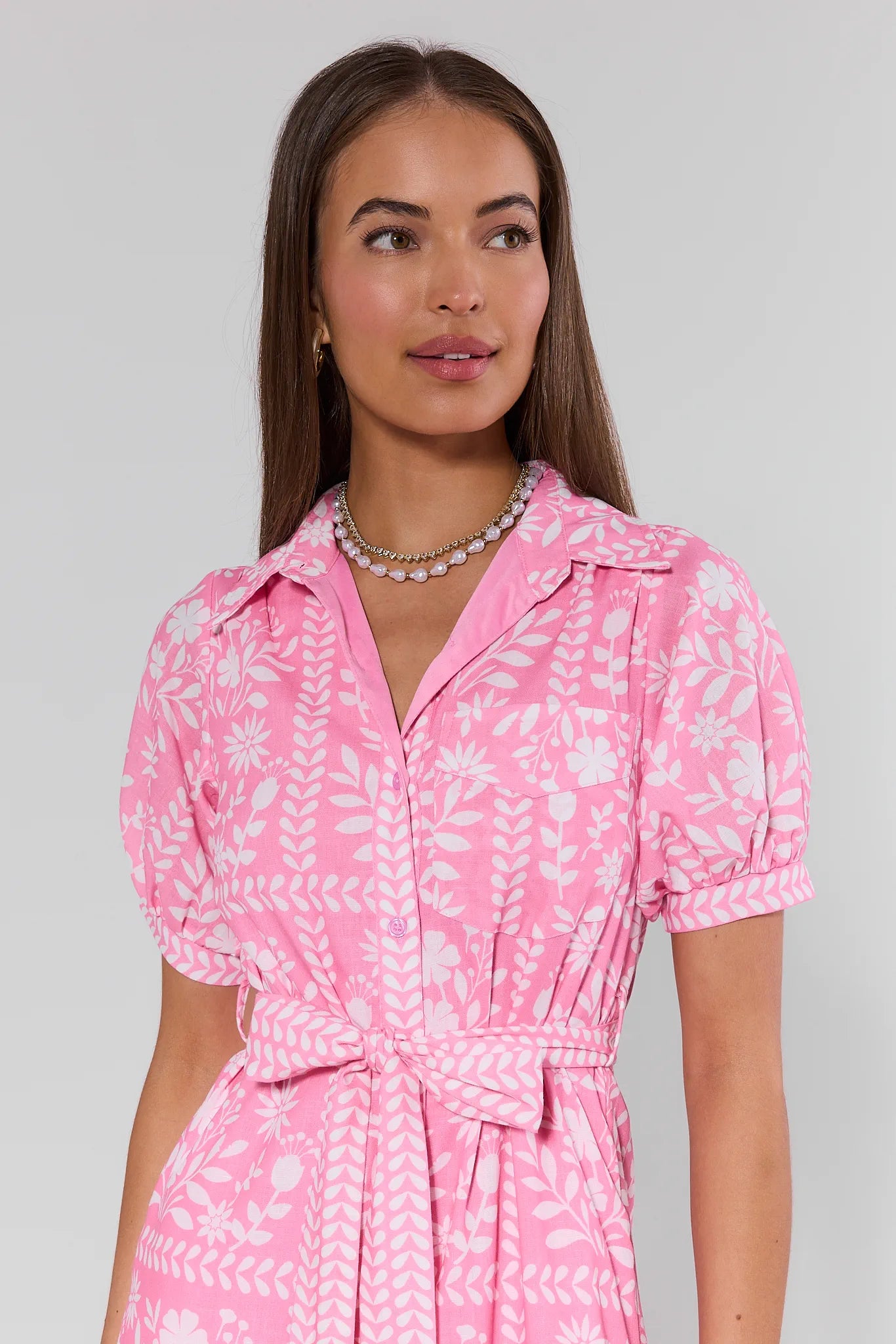 Woman wearing a pink dress with white floral pattern on a gray background